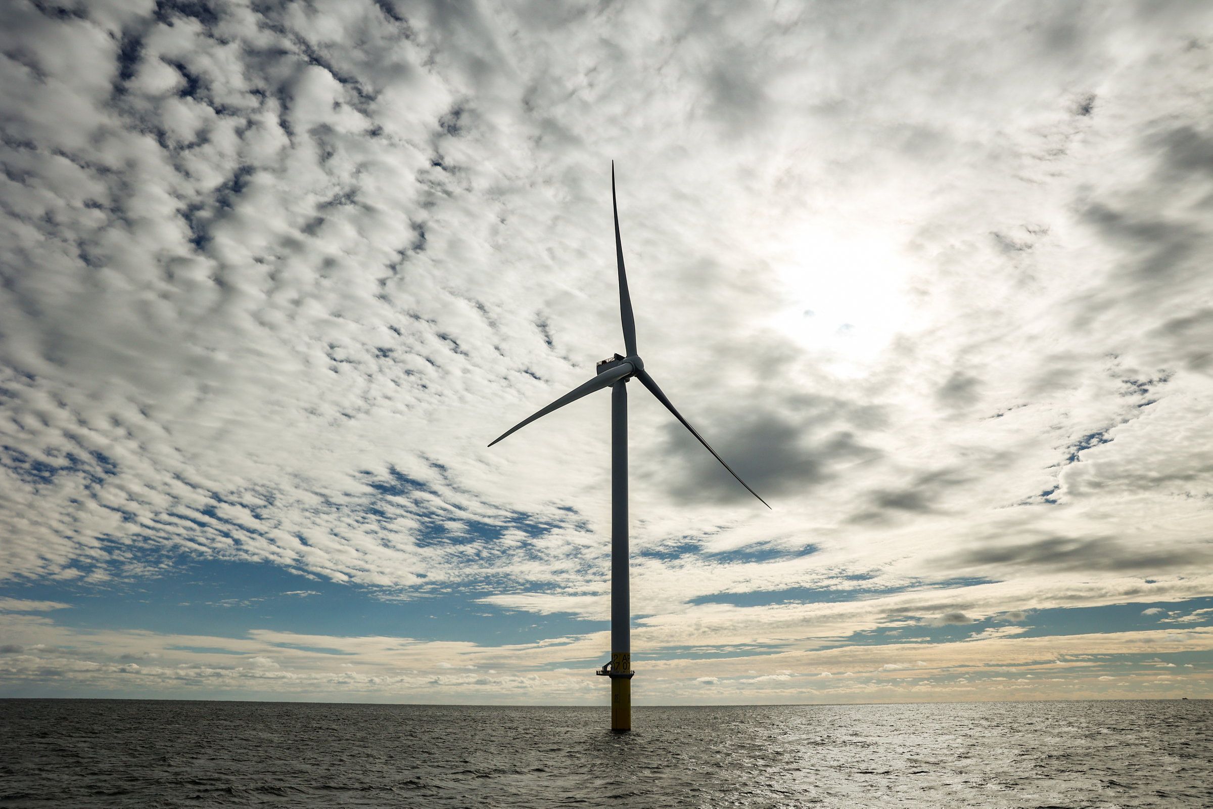 A single wind turbine stands above the sea.