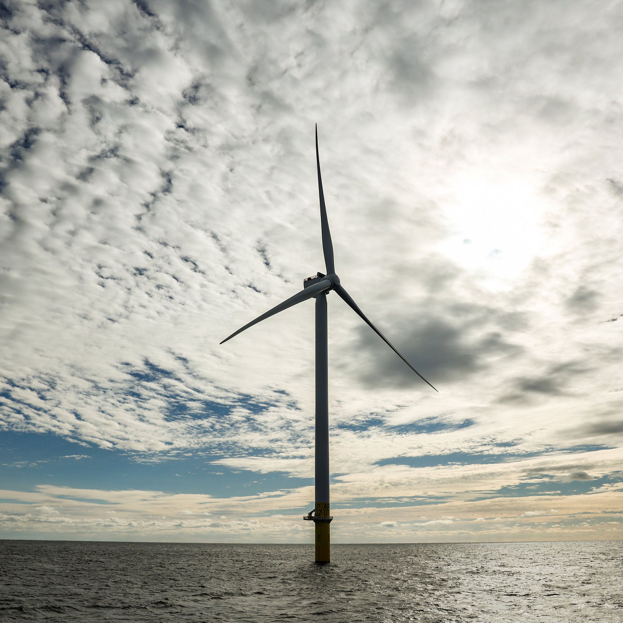 A single wind turbine stands above the sea.