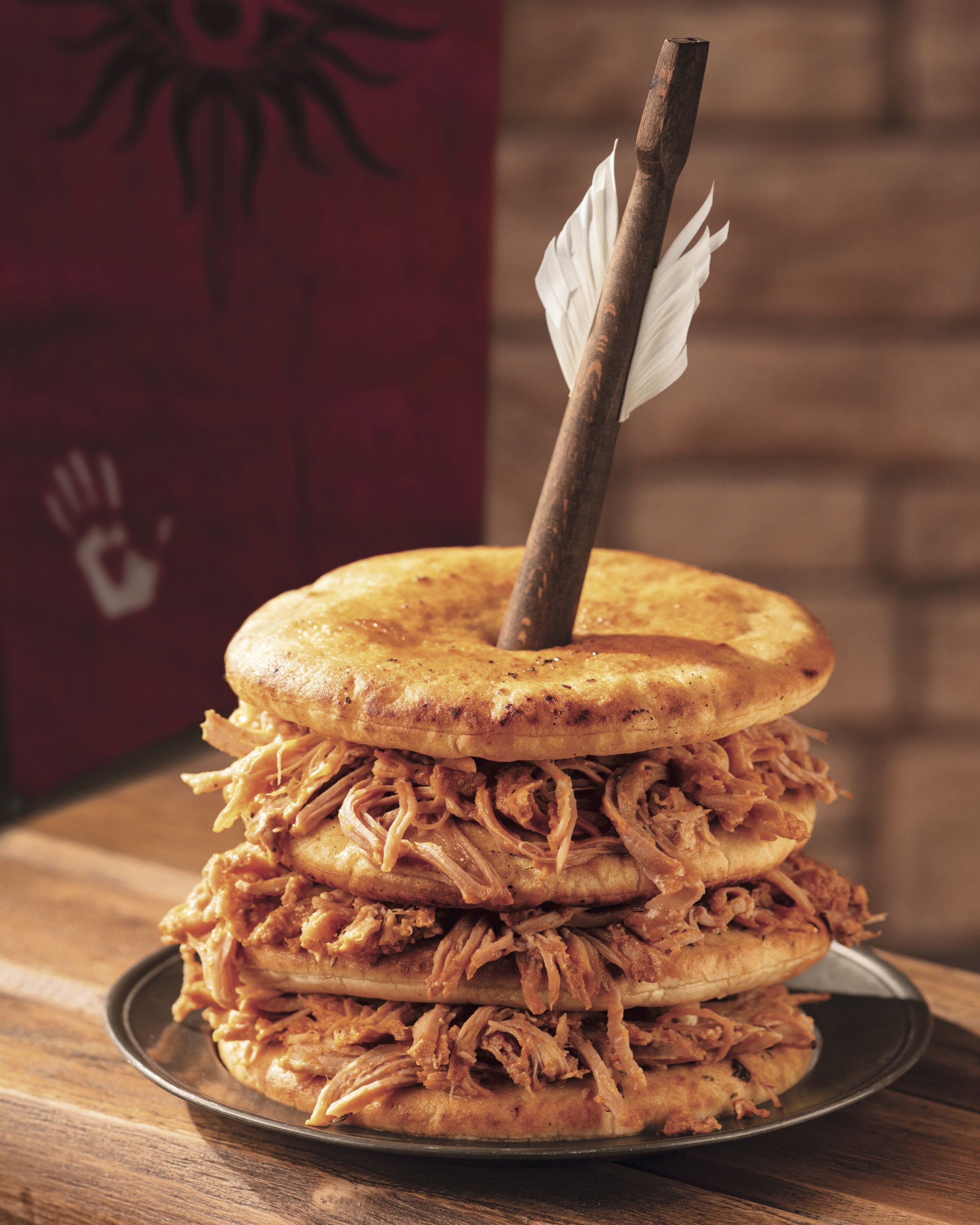A stack of savory pancakes with pulled pork between each layer, and a crossbow bolt protruding from the stack.