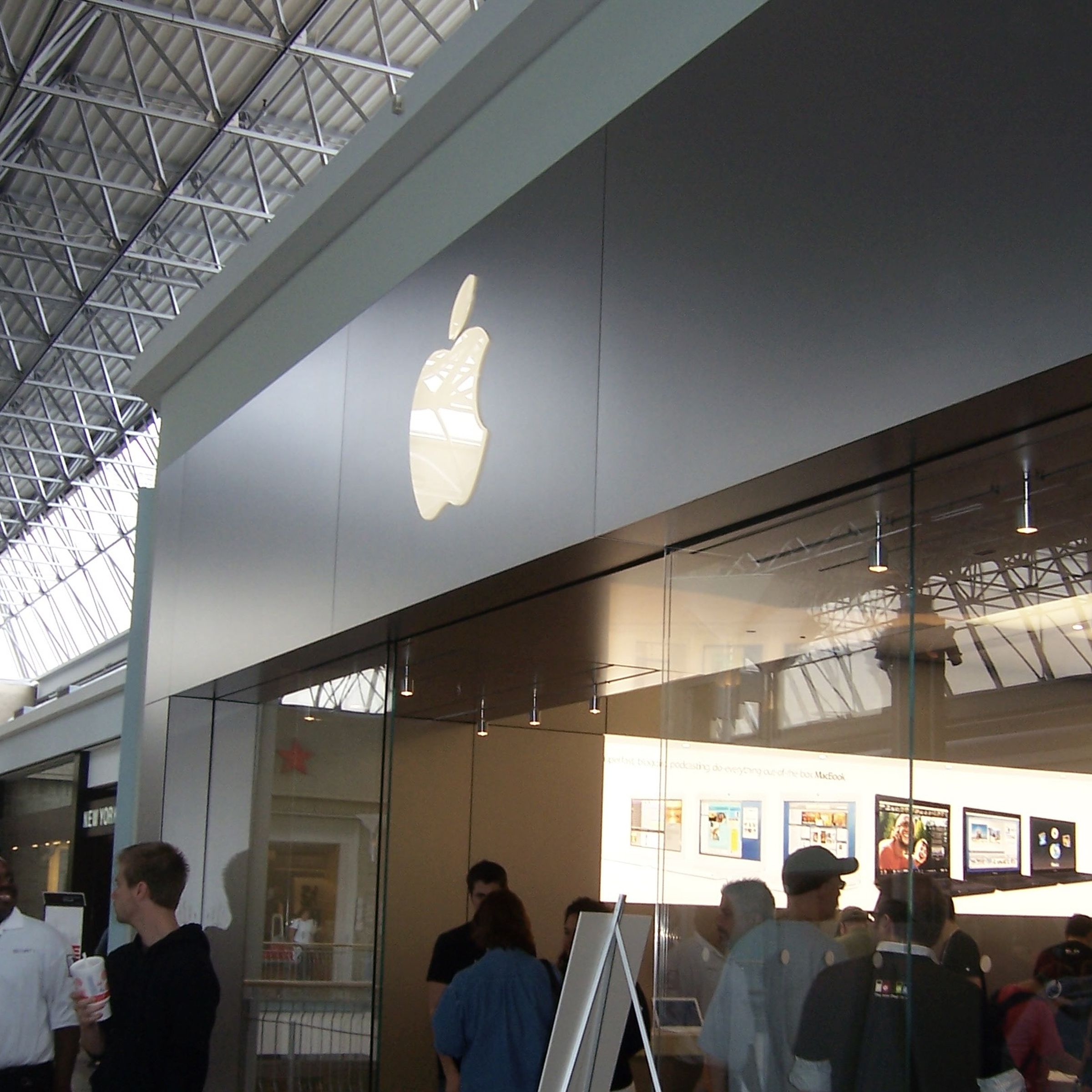 Apple Store front in mall with lit apple logo on top and many people inside