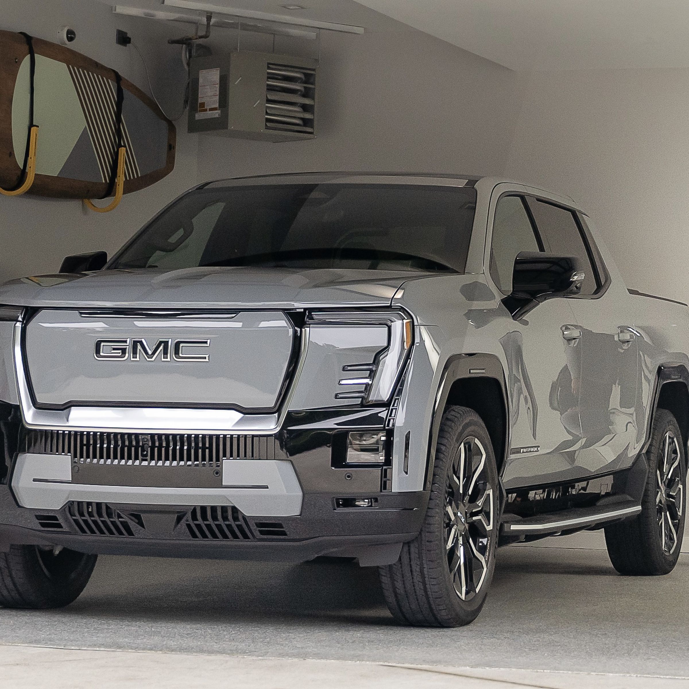 Silver GMC truck in a garage with a kayak on the wall and a person holding the charge plug on the side of the truck