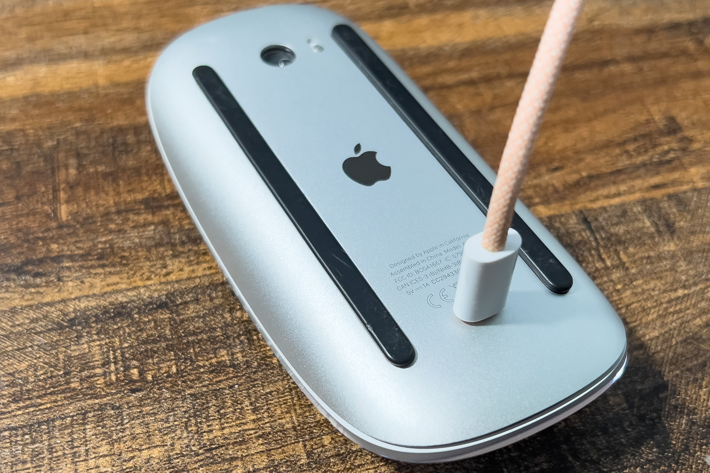 A picture of a Magic Mouse laying on its back with a lightning cable plugged into it.