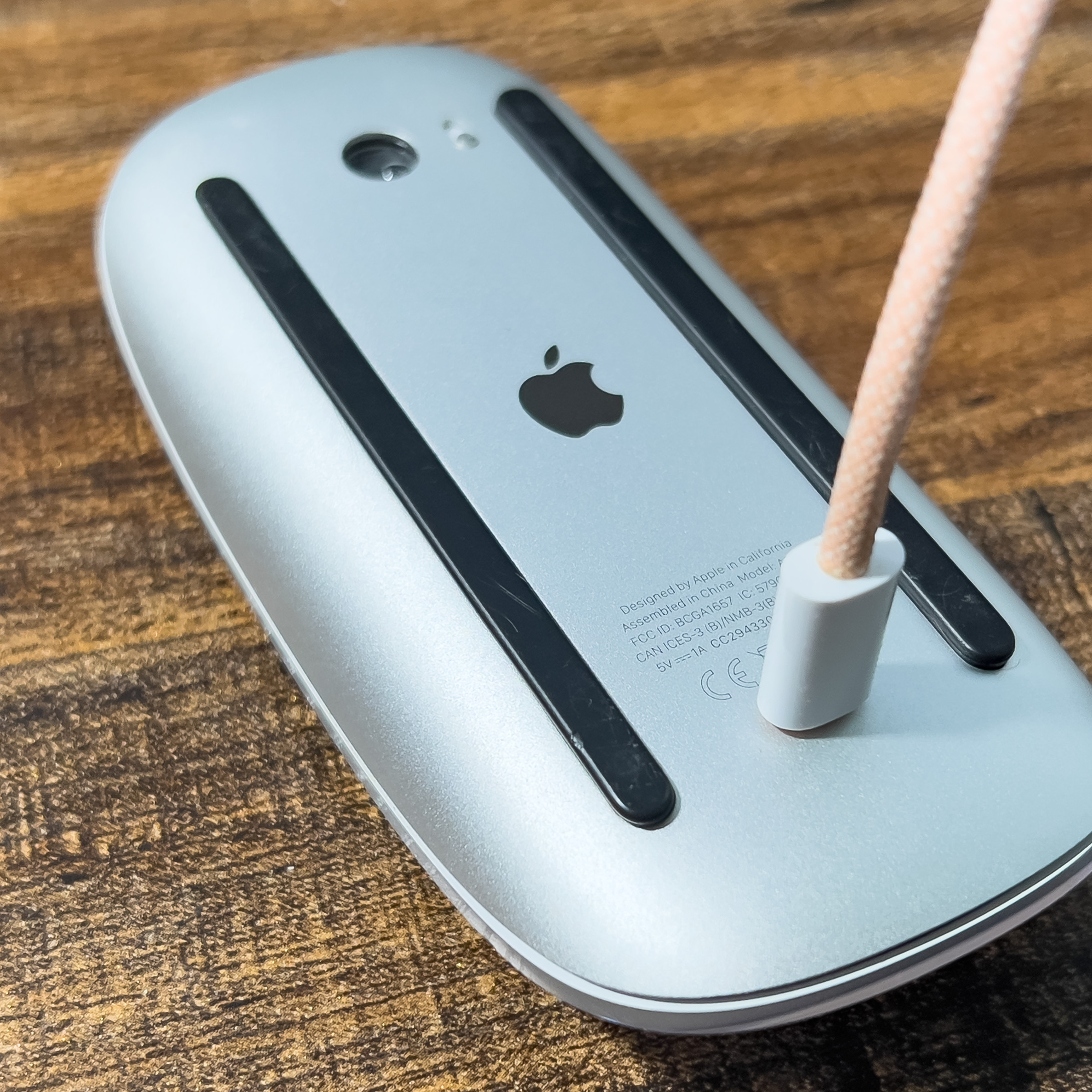 A picture of a Magic Mouse laying on its back with a lightning cable plugged into it.