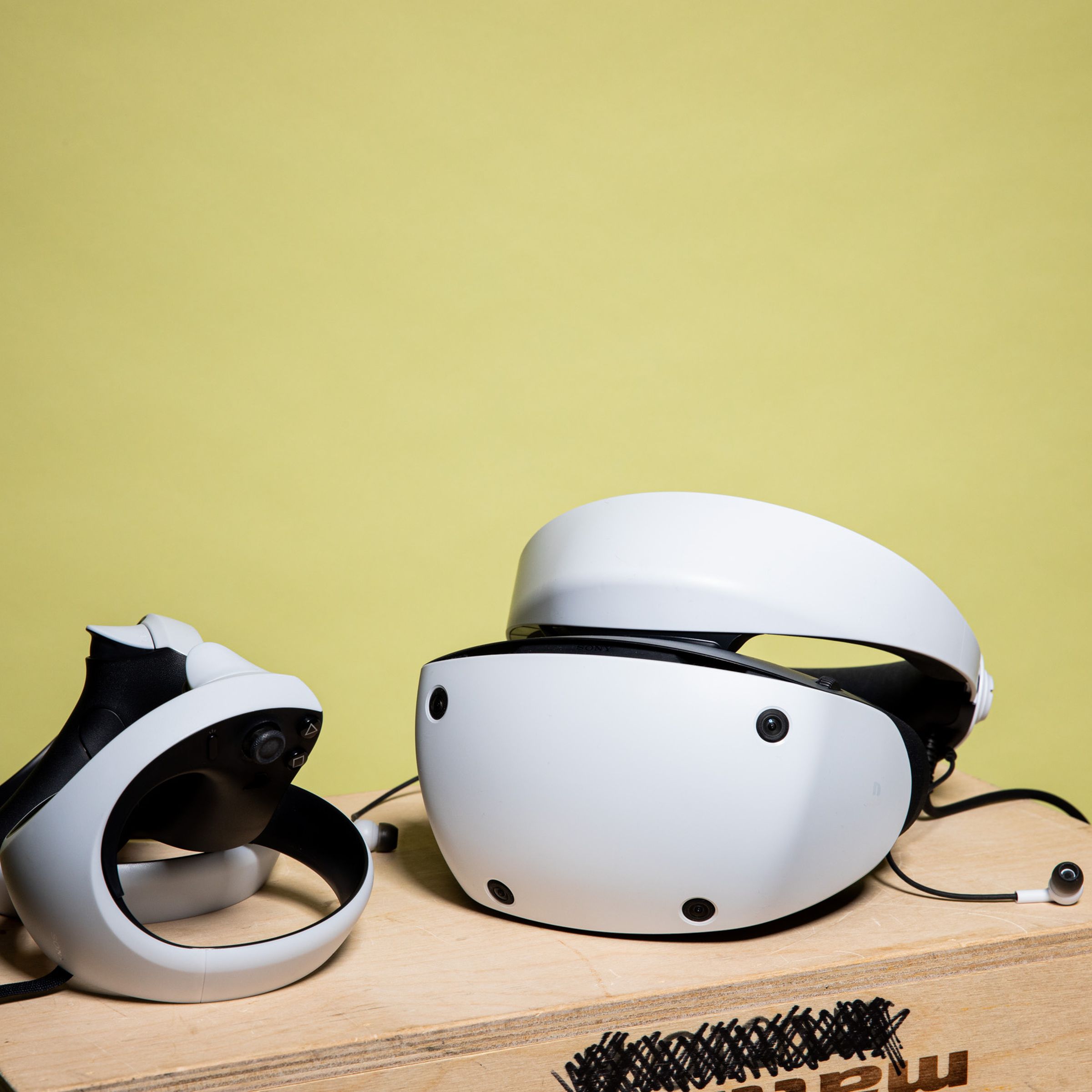 The headset and controllers sit on a wooden box, earbuds dangling out.