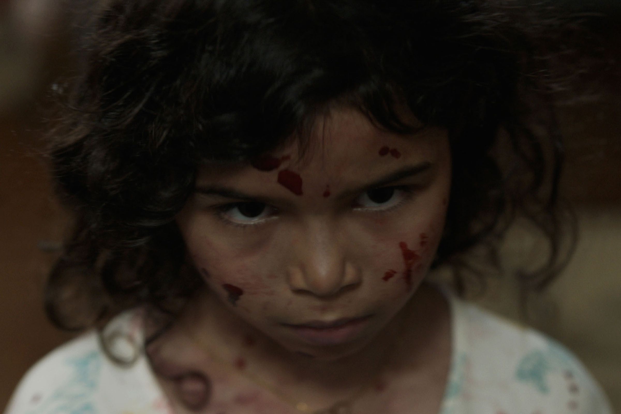A little girl with a stern downturned faced that’s flecked with blood.