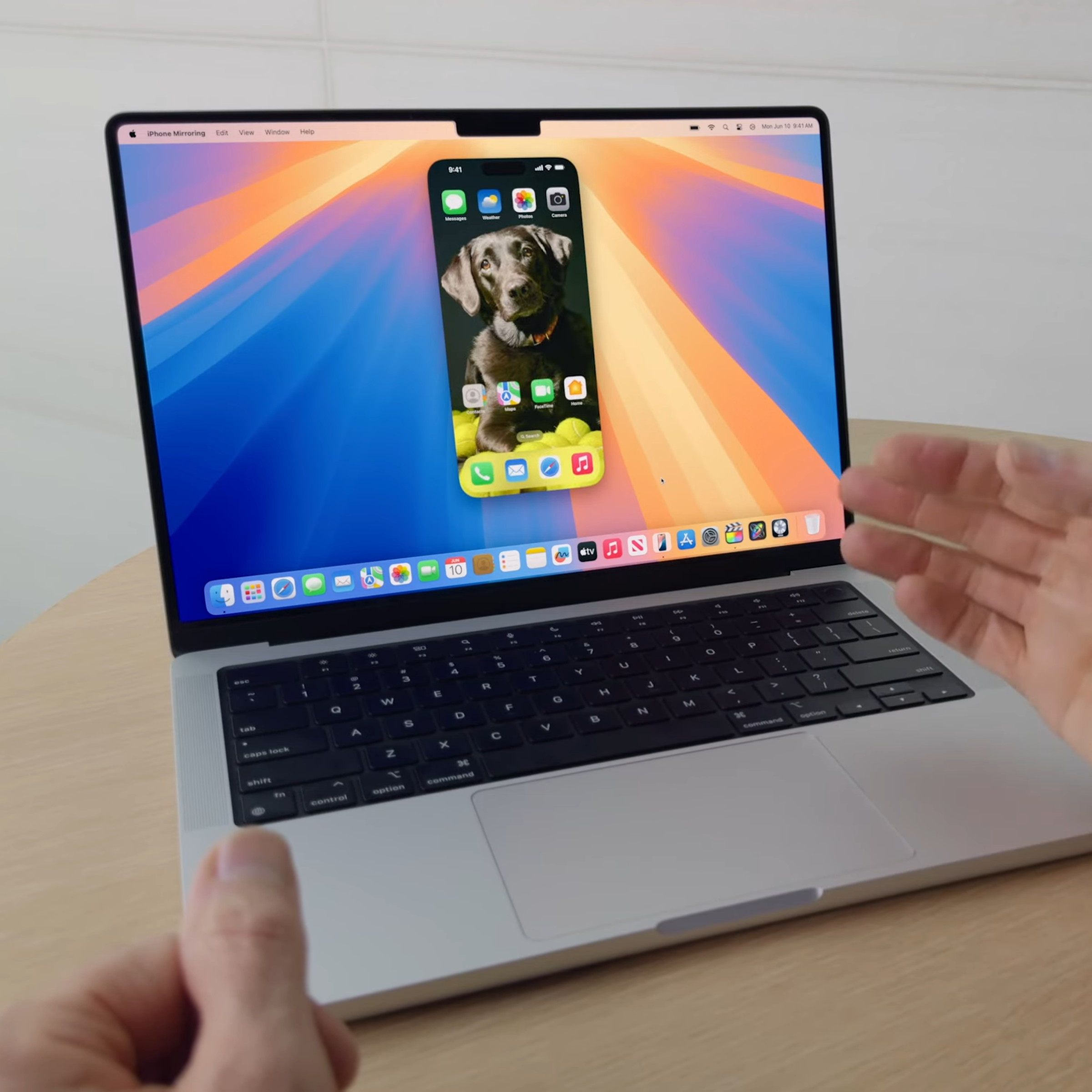 A MacBook Pro on a table shows a mirrored iPhone on its screen.