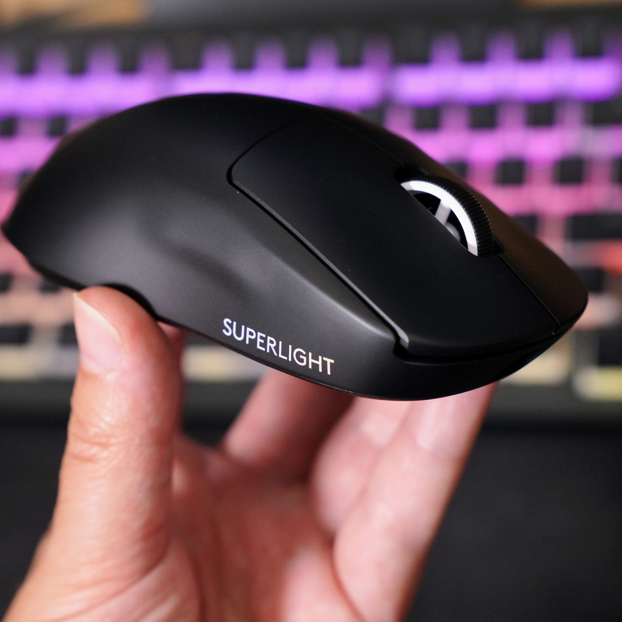 A hand holds up a jet black sculpted plastic mouse with a white scroll wheel and white words “Superlight” printed on the side.