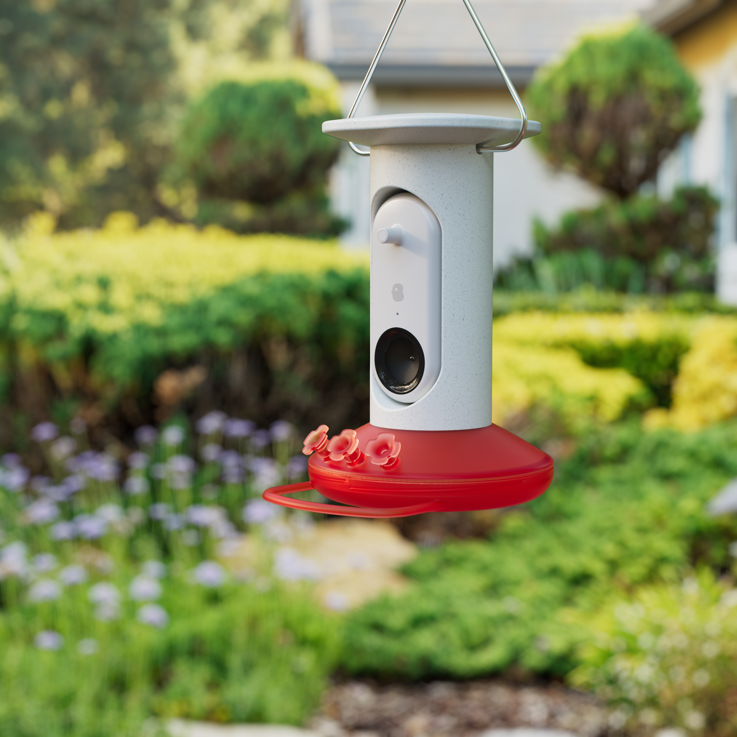 Picture of the Bird Buddy Smart hummingbird feeder hanging up in front of some flowers.