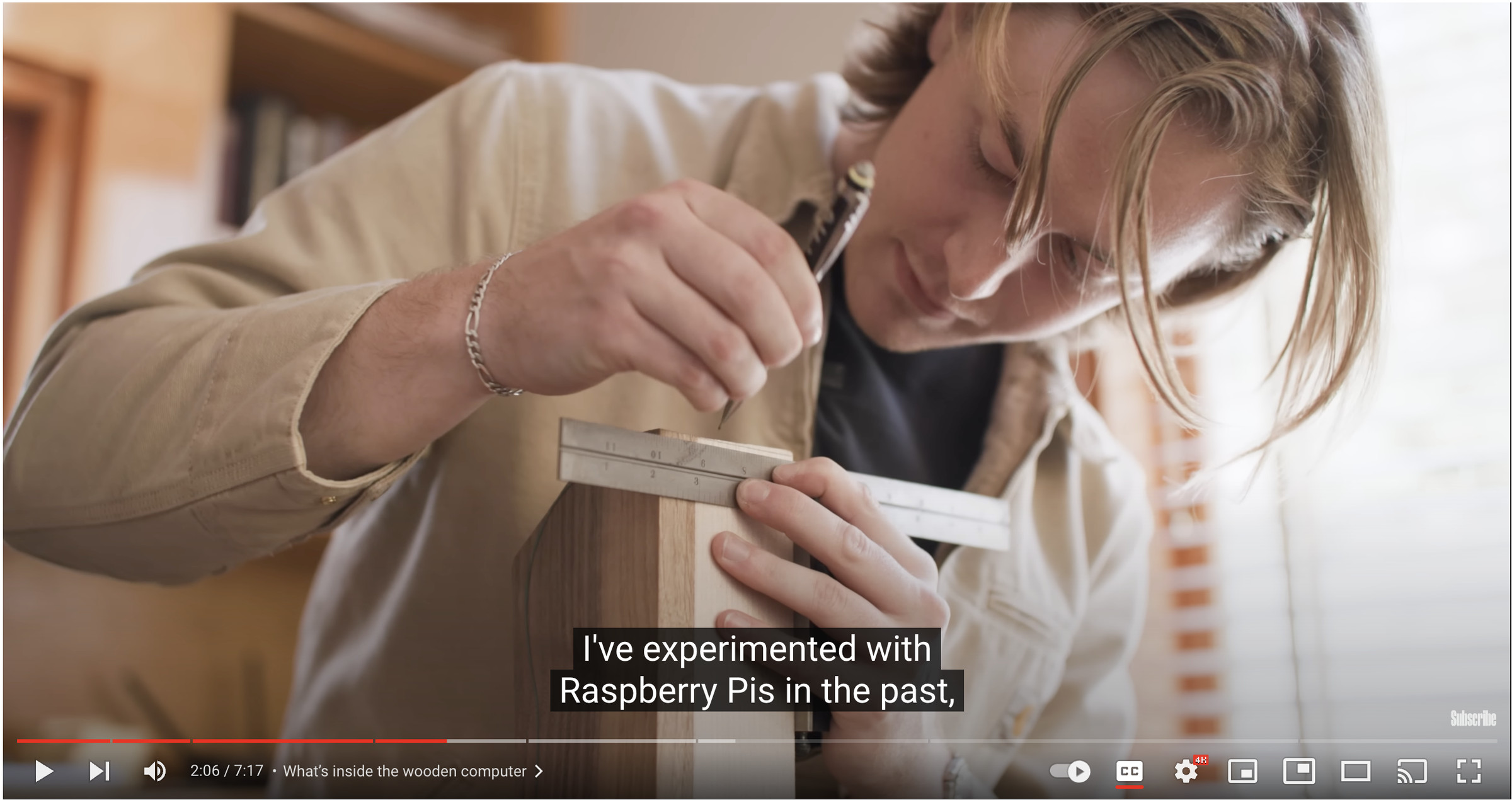 Screenshot of a YouTube video from The Verge showing a man using a straight edge to make marks on a piece of hardwood. The YouTube overlay and closed captions are visible.