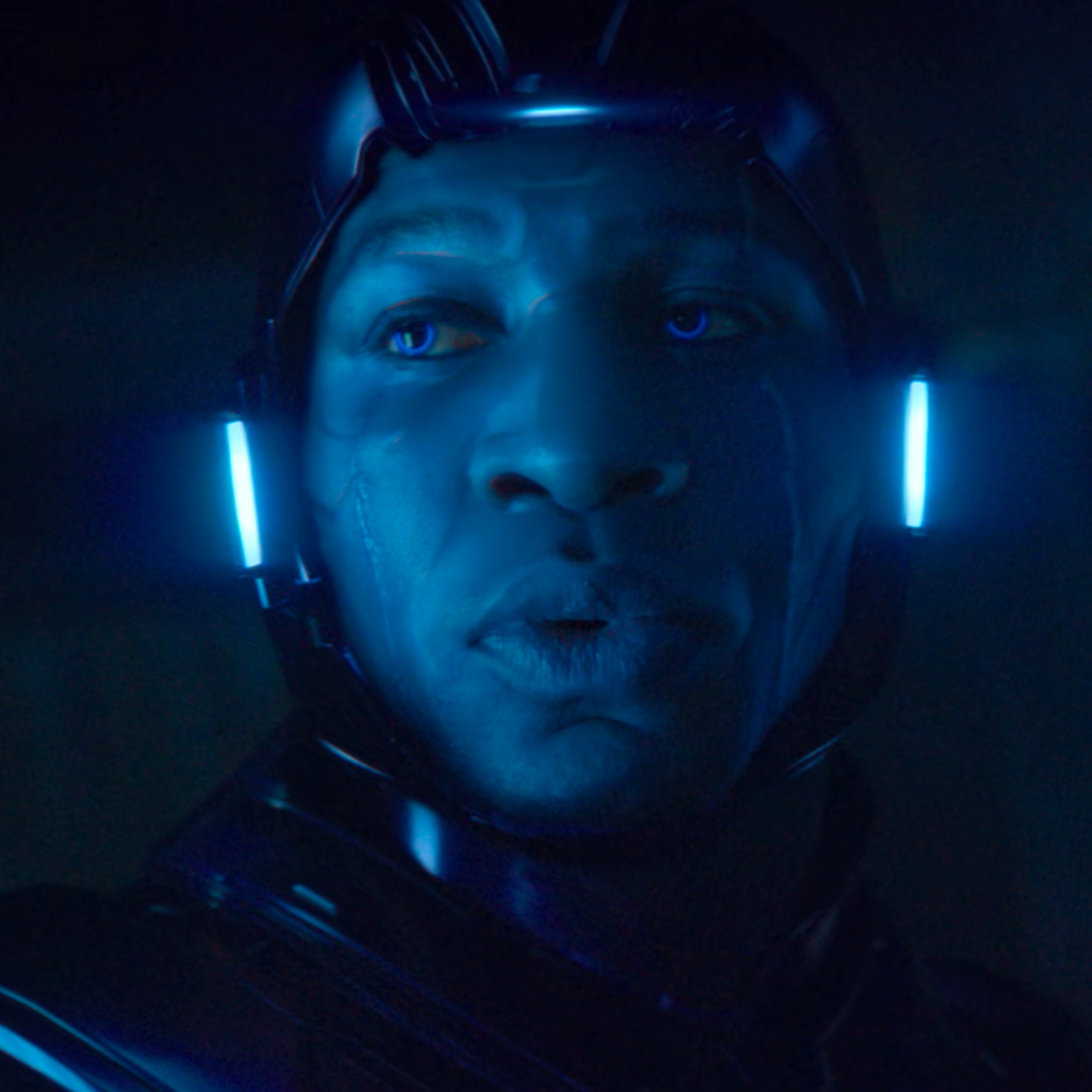 A tight shot of a man wearing a formfitting helmet that casts a translucent blue sheen over his face, which is visible from his hairline down to his chin.