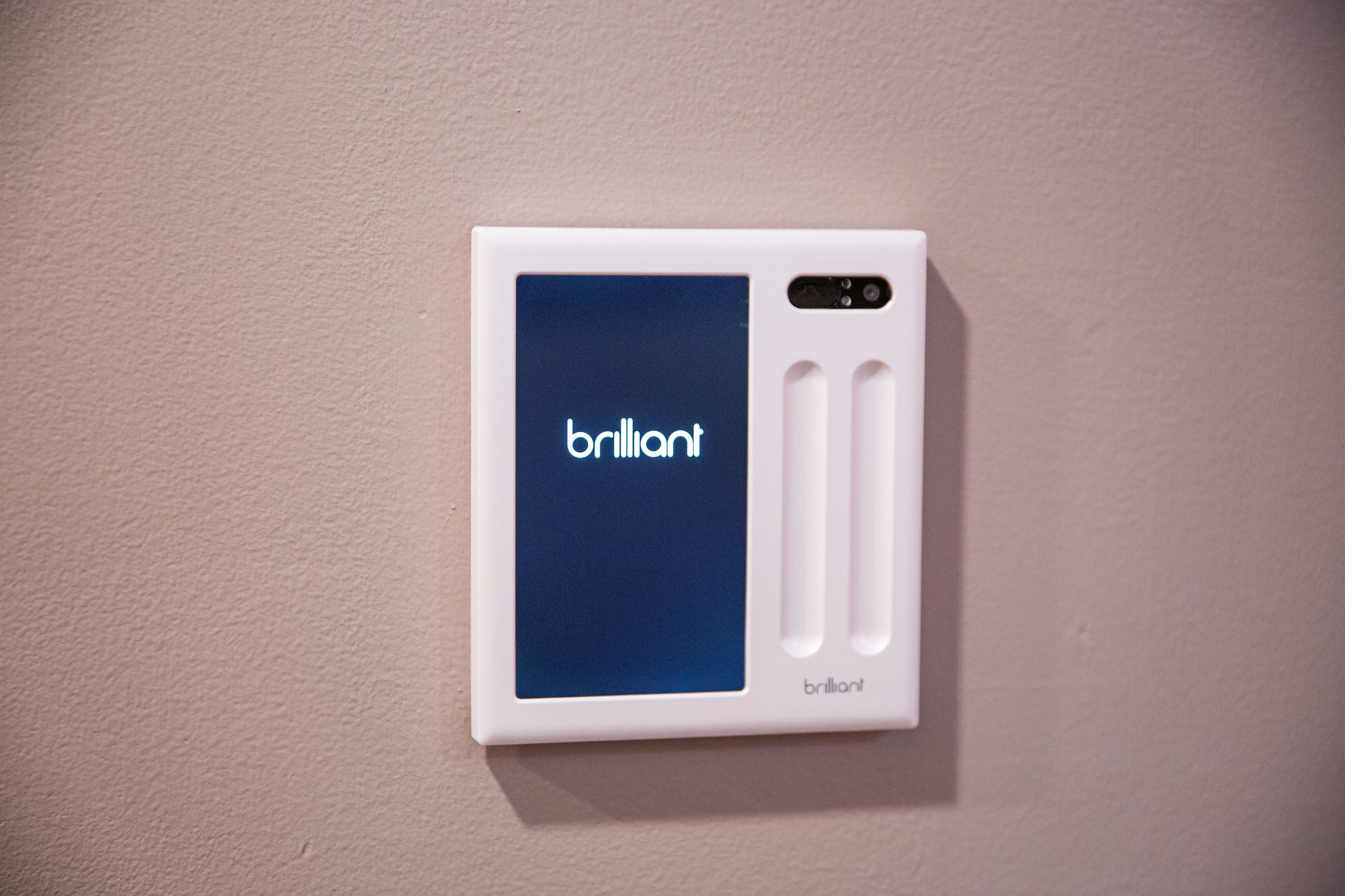 A touchscreen smart home panel on a wall with the word Brilliant displayed.