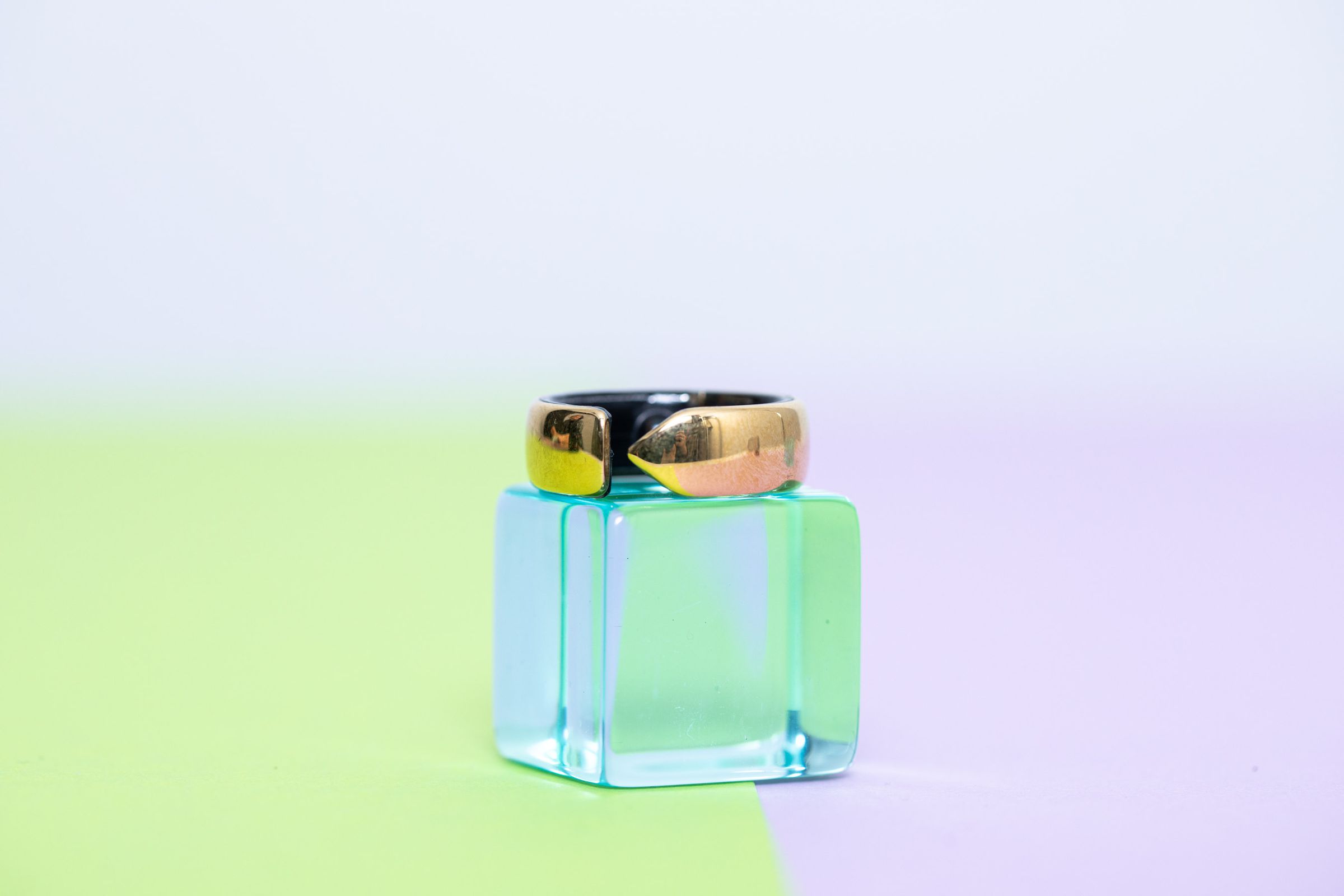 The Evie Ring on top of a clear blue block on top of a pastel green and purple background.