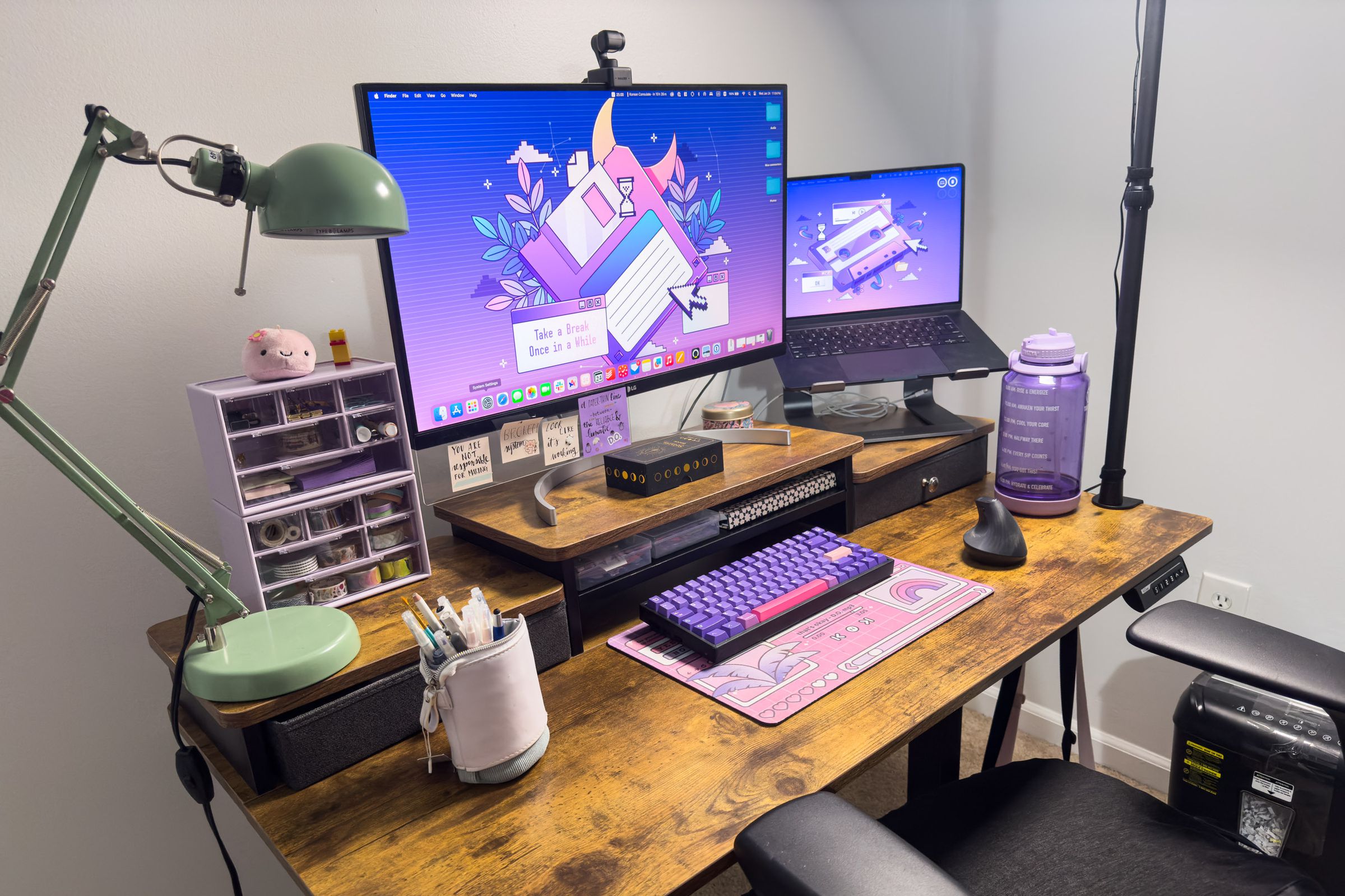 Desk with monitor, lamp in foreground, purple keyboard.