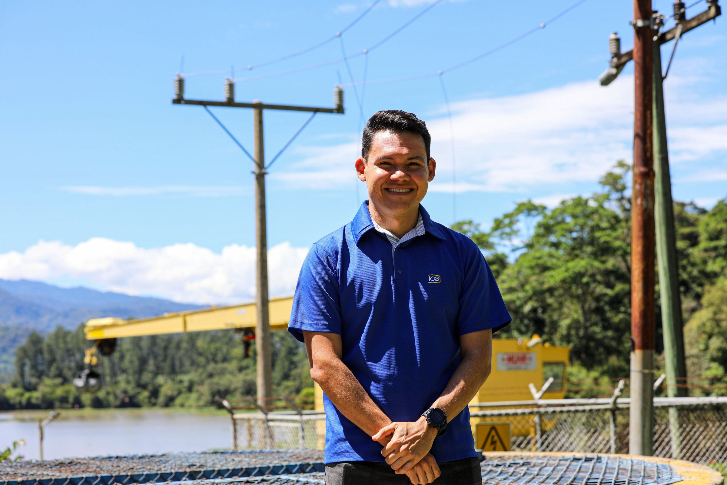 A smiling man stands in front of electric power lines.