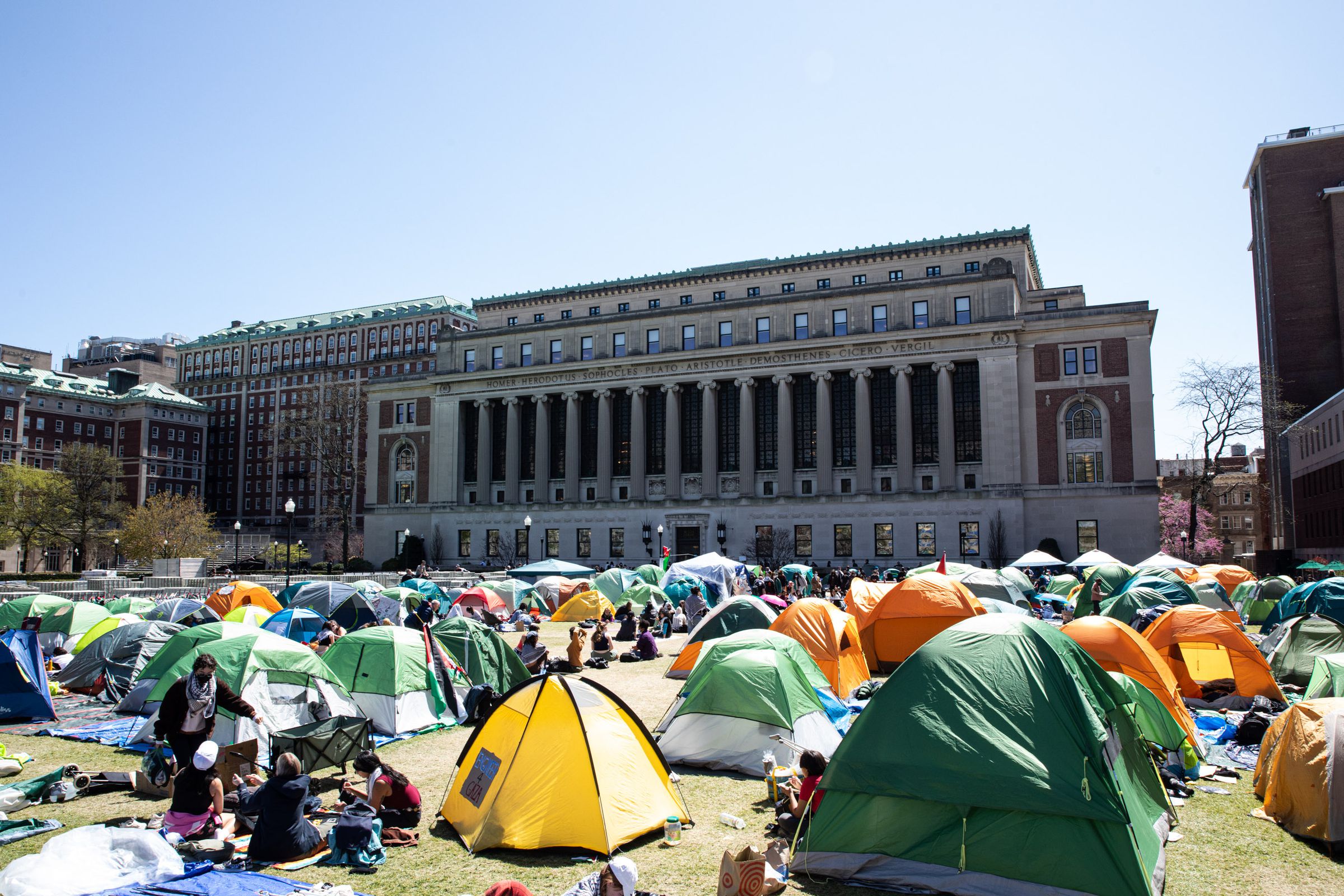 The tents of a student encampment at Columbia University spread out across the quad. The library, a building with neoclassical columns, looms in the background.