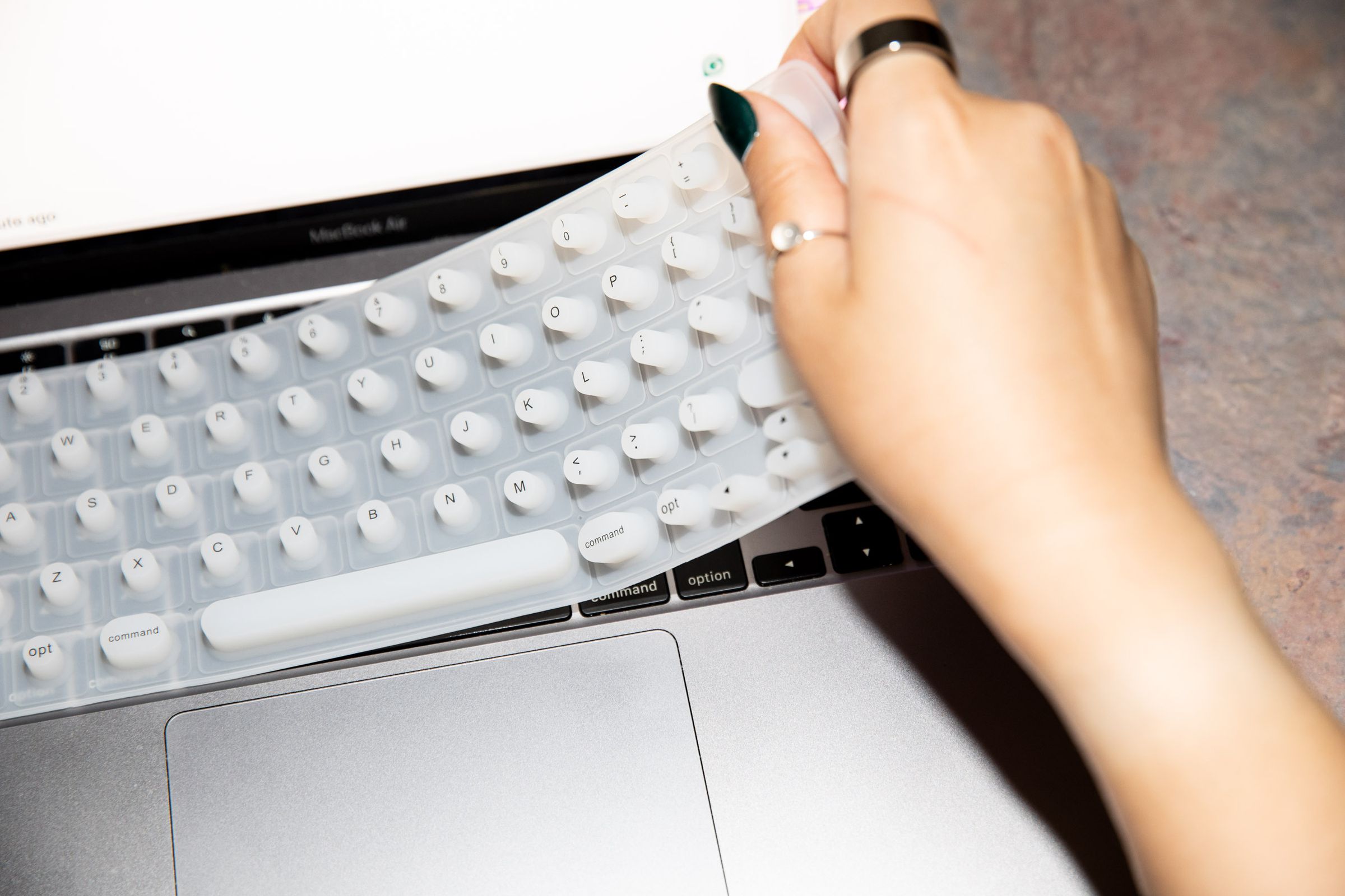 Person with long nails placing keyboard cover over laptop