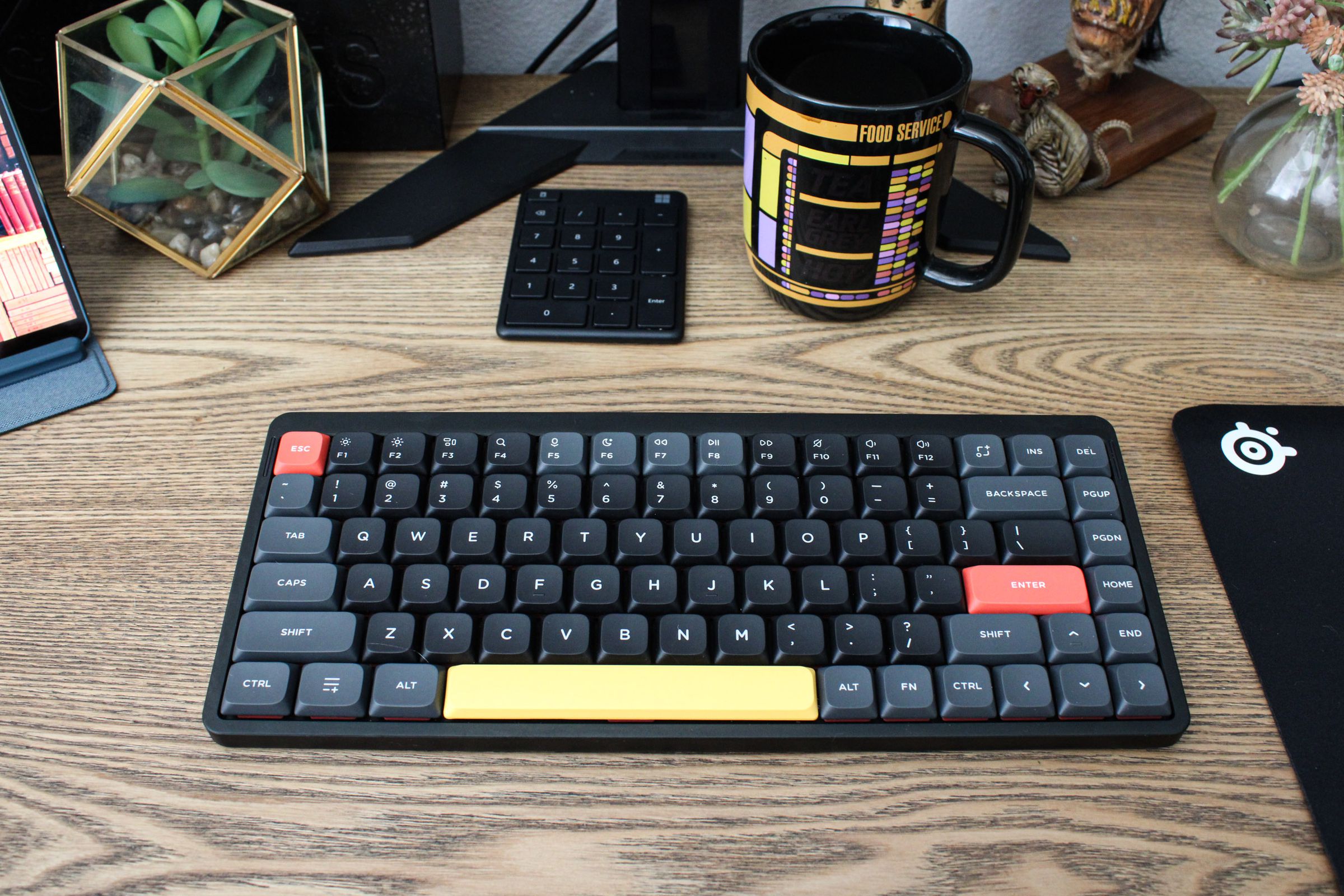 A Nuphy Air75 V2 keyboard with black, gray, red and yellow keys on a desktop.
