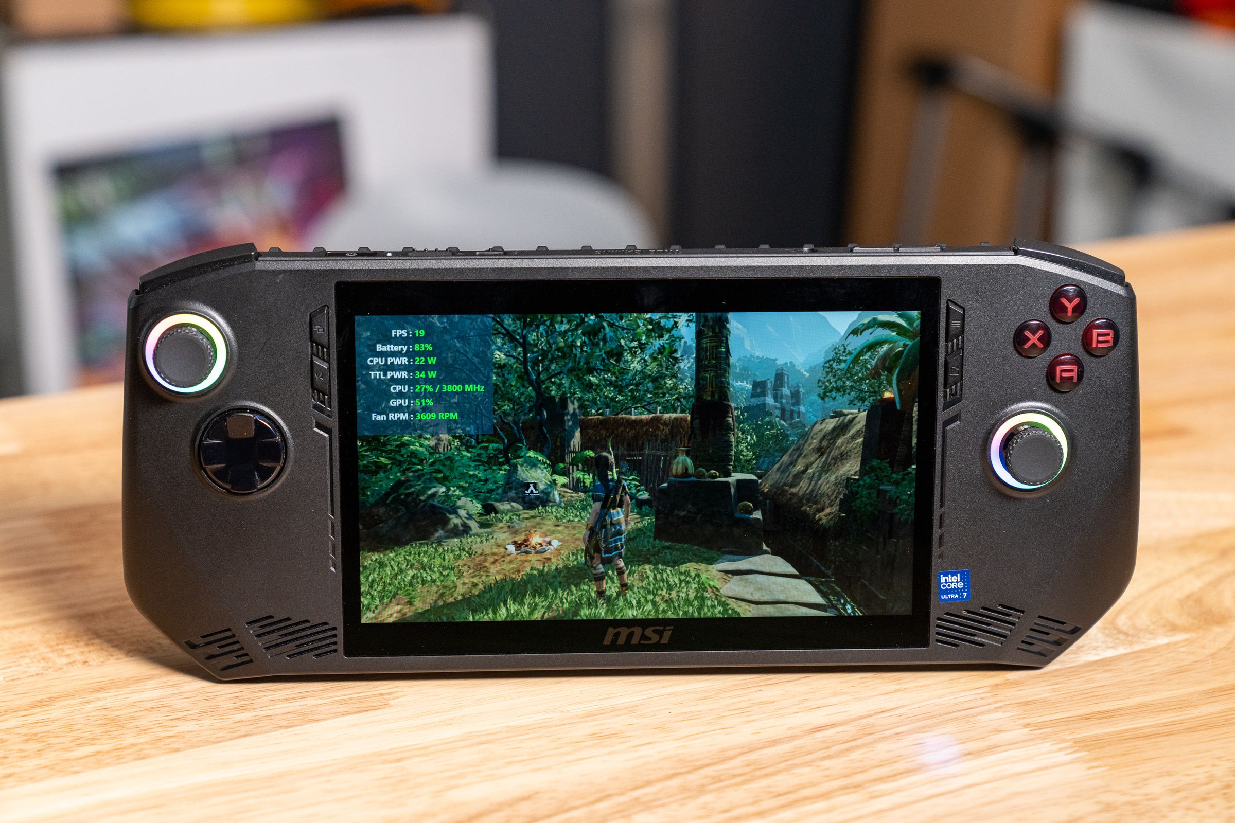 A black wide handheld gaming PC with rainbow rings around its black joysticks and Tomb Raider on the screen.