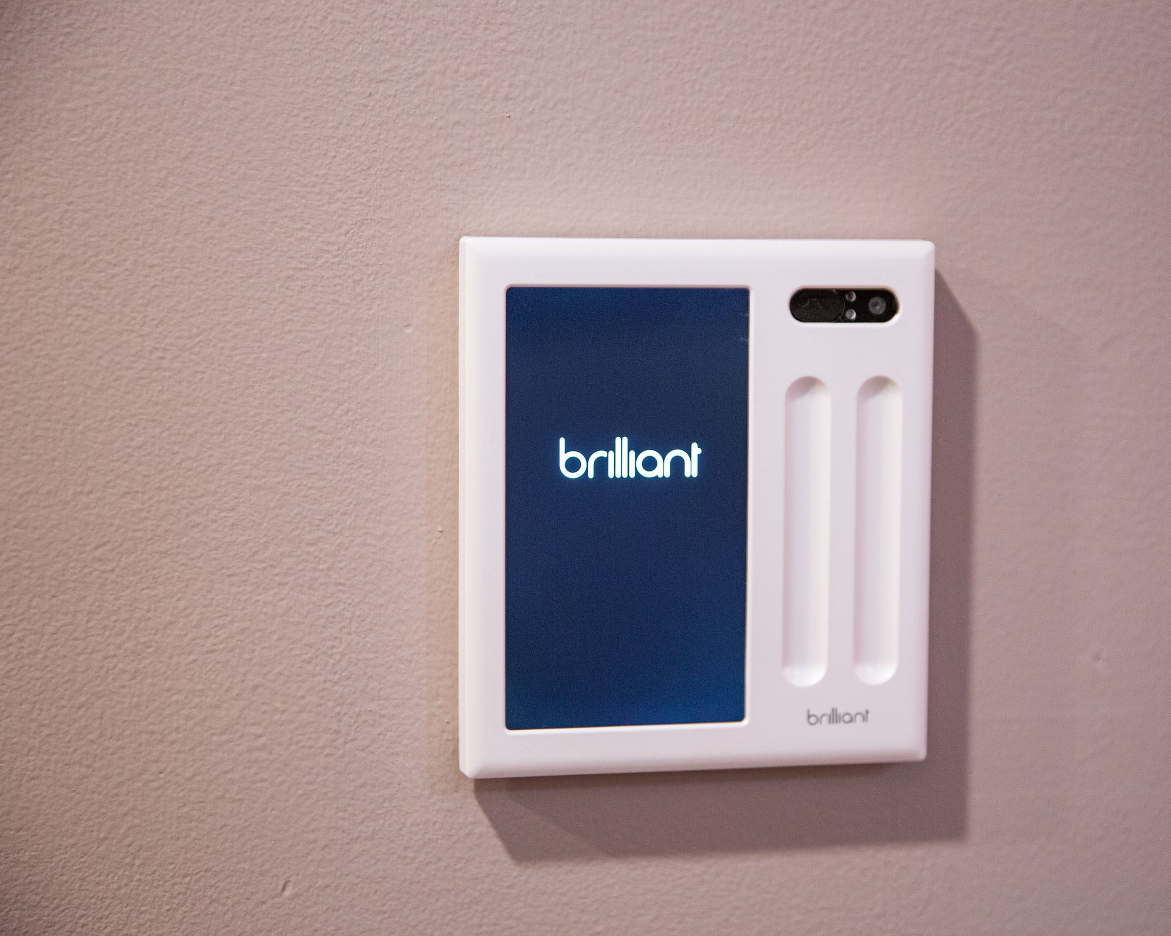 A touchscreen smart home panel on a wall with the word Brilliant dispalyed.