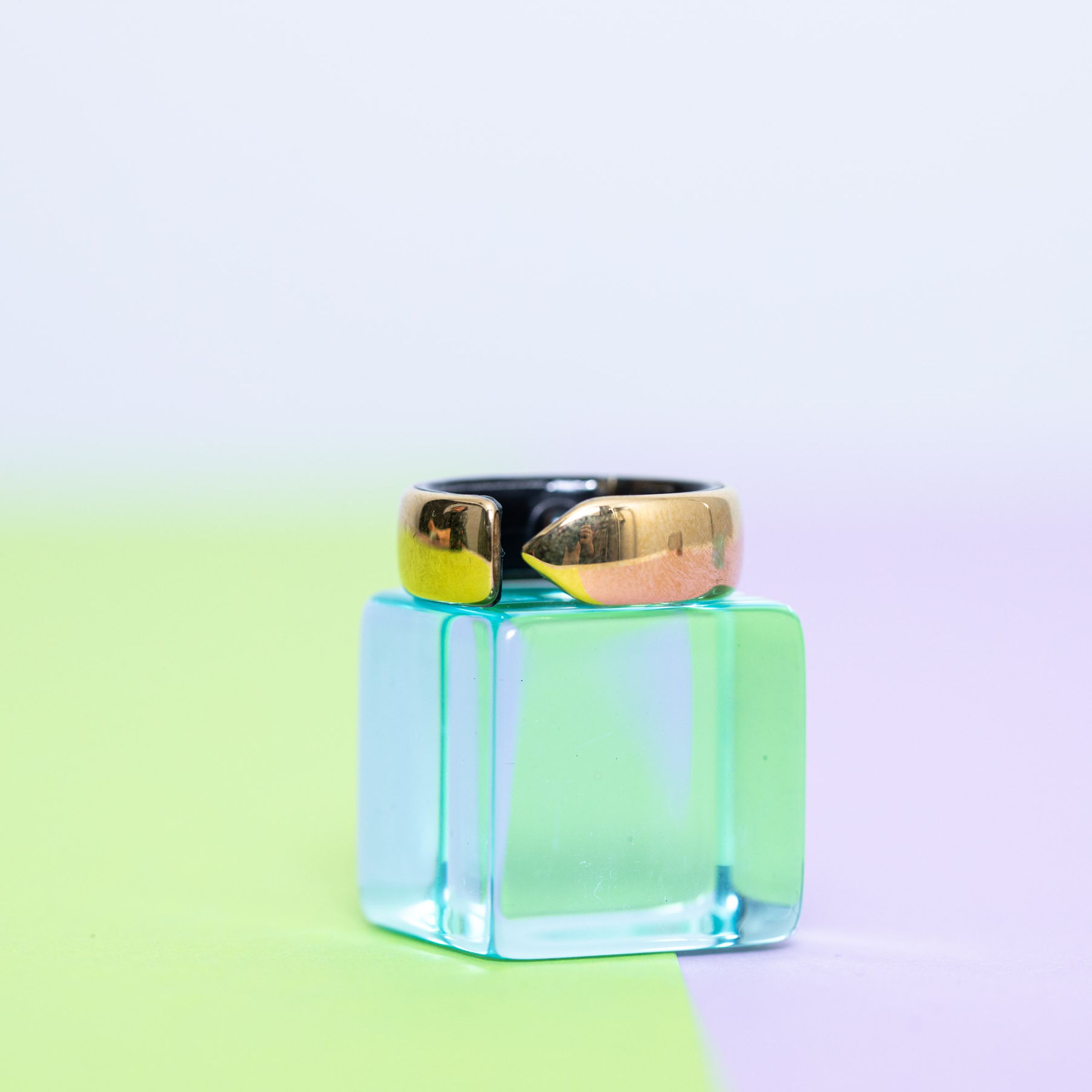 The Evie Ring on top of a clear blue block on top of a pastel green and purple background.