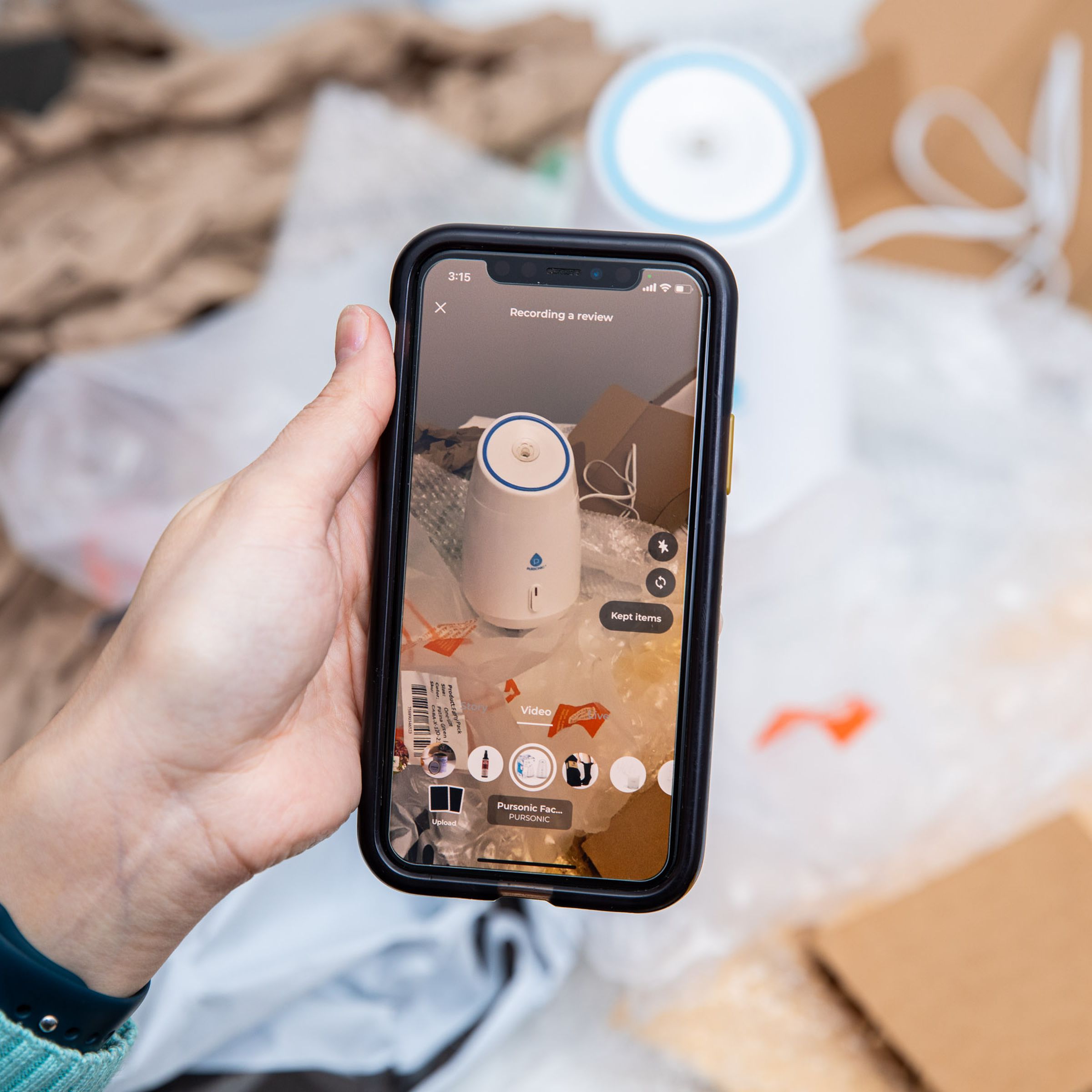 A phone recording a video review of products. In front of the screen is a mess of wrapping, boxes, and products strewn about. 