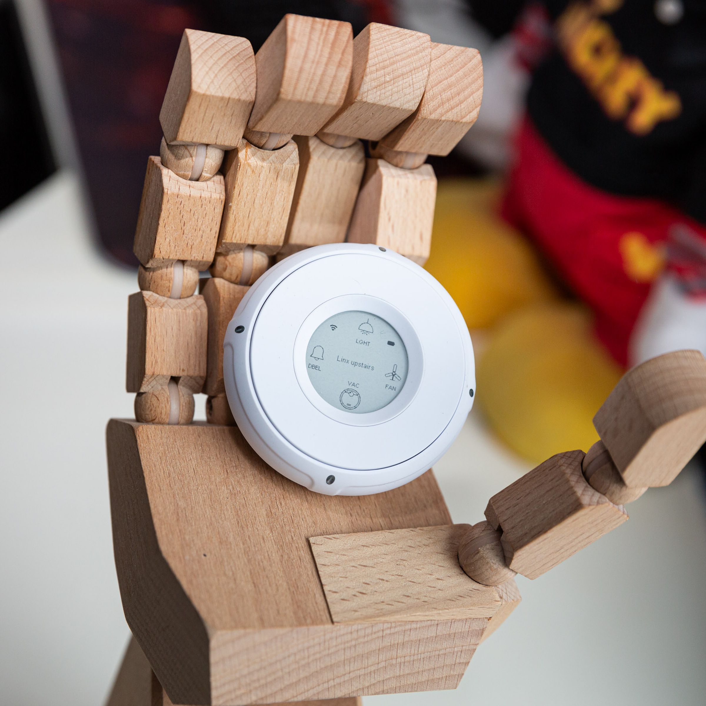 A white smart button with an e-paper screen in a wooden model hand on a desk.