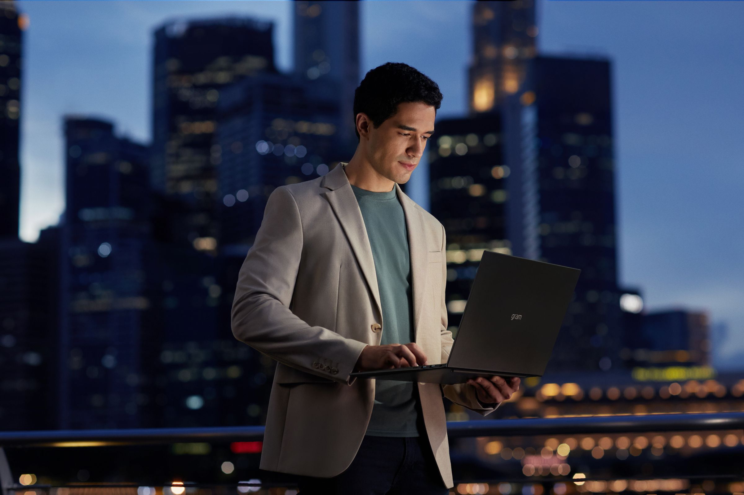 A user works on an LG Gram laptop at night in an urban cityscape setting.