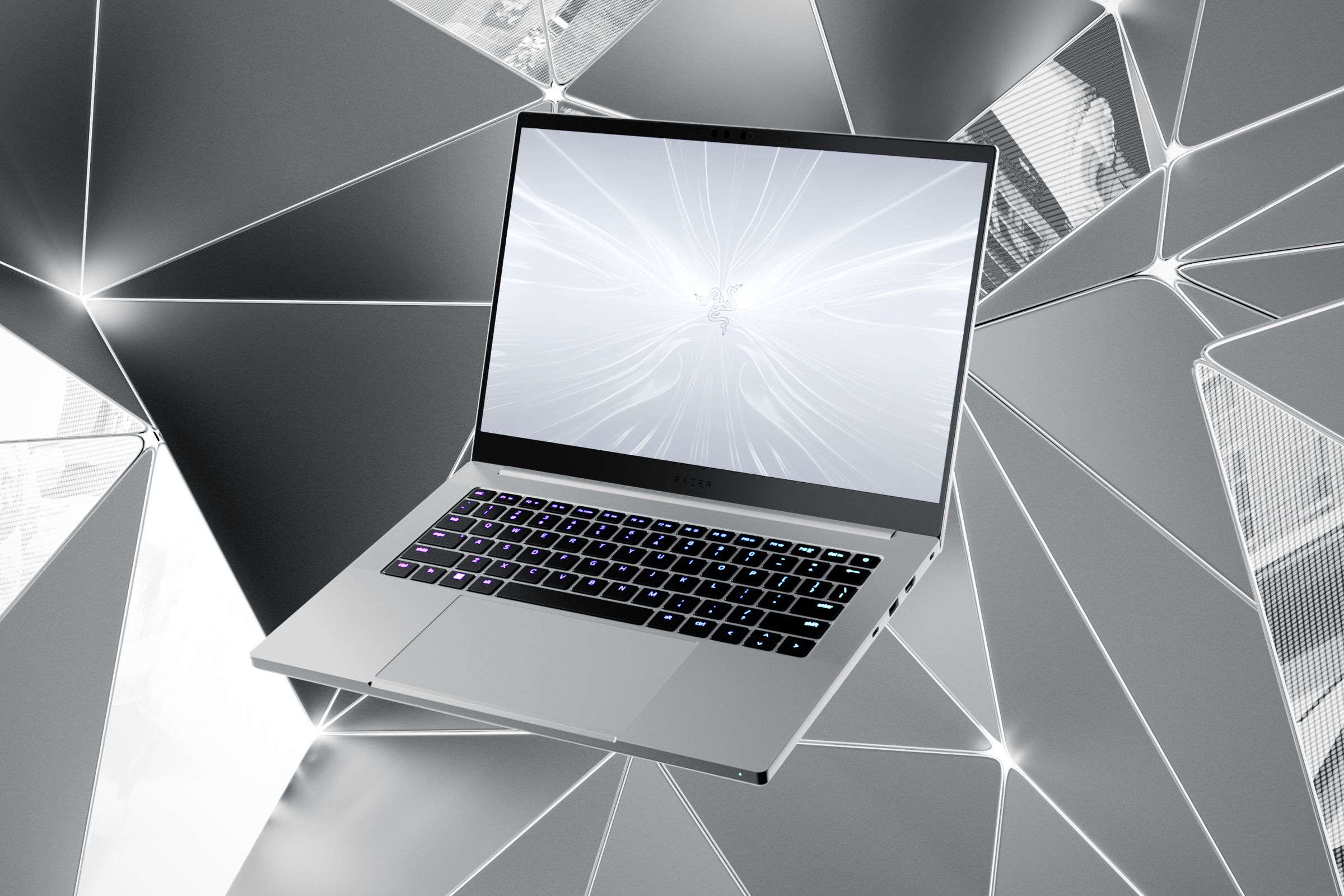 Razer Blade 14 gaming laptop, in silver, on a stylized background. It is a silver-colored laptop, not unlike a MacBook Air, with a black keyboard with visible RGB backlighting.