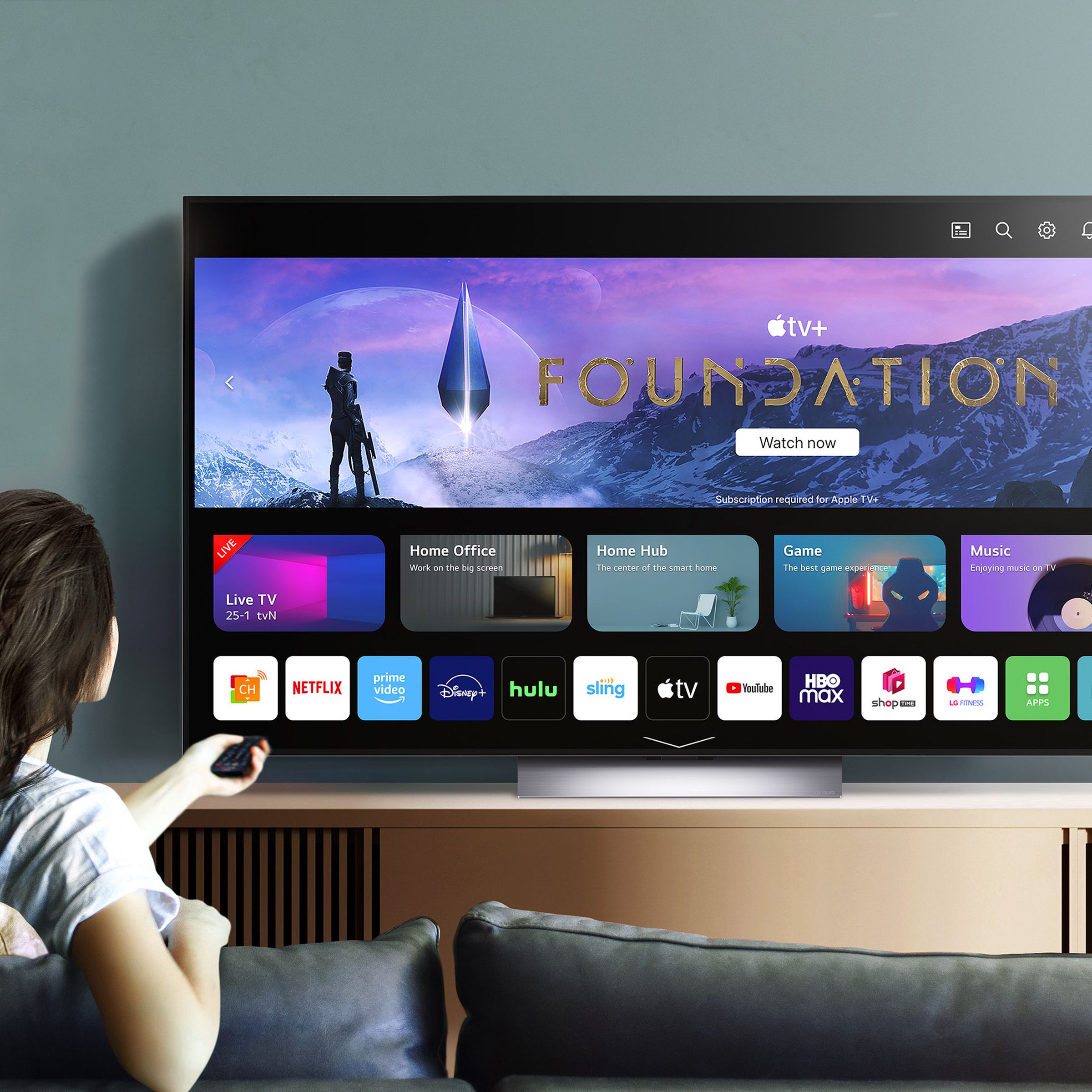 An image of an LG OLED TV on the home screen with a person sitting on a couch in front.