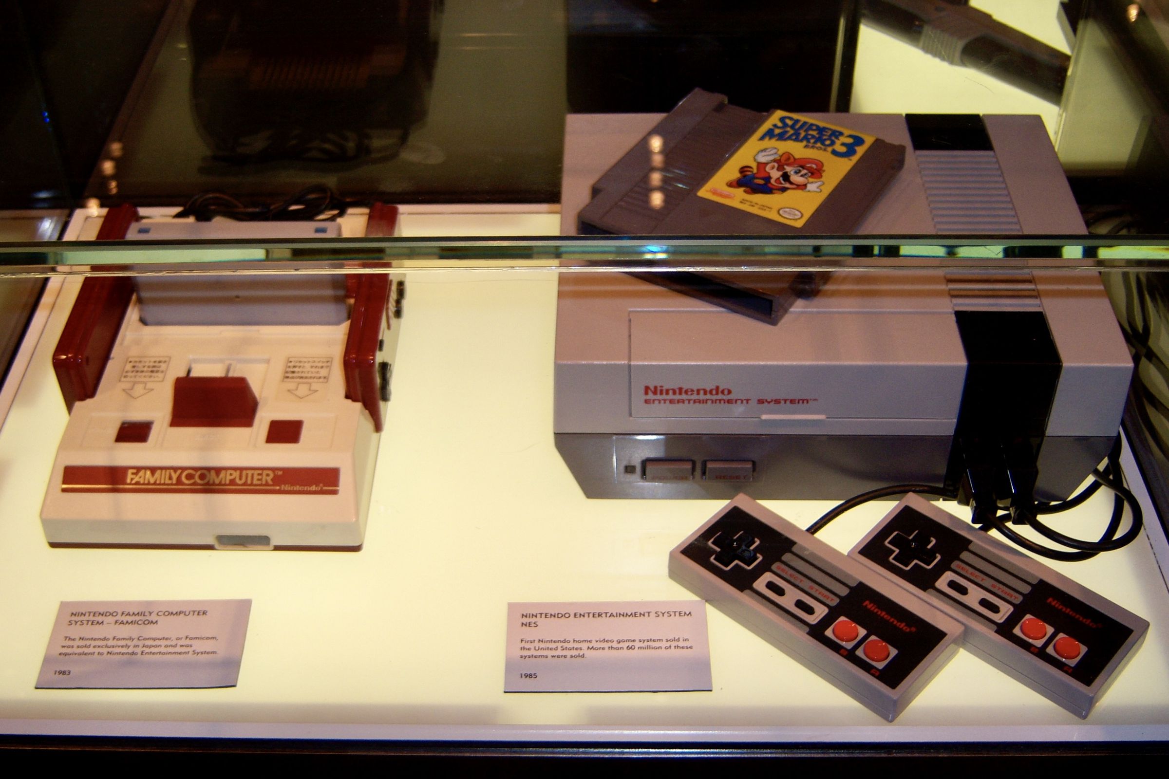 Nintendo world in NYC display for Nintendo Famicom and NES systems. There are two controllers hooked up to the NES and a Mario Bros. 3 cartridge on top.