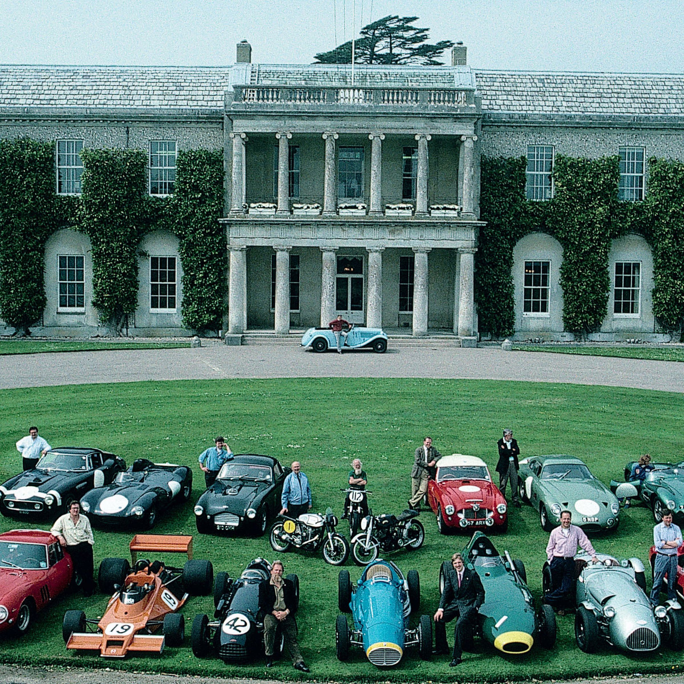 The cast of cars and characters from the first Goodwood press day in 1993. Lord Charles March is by the front door of the house with his light blue AC 16/80 designed by his grandfather.