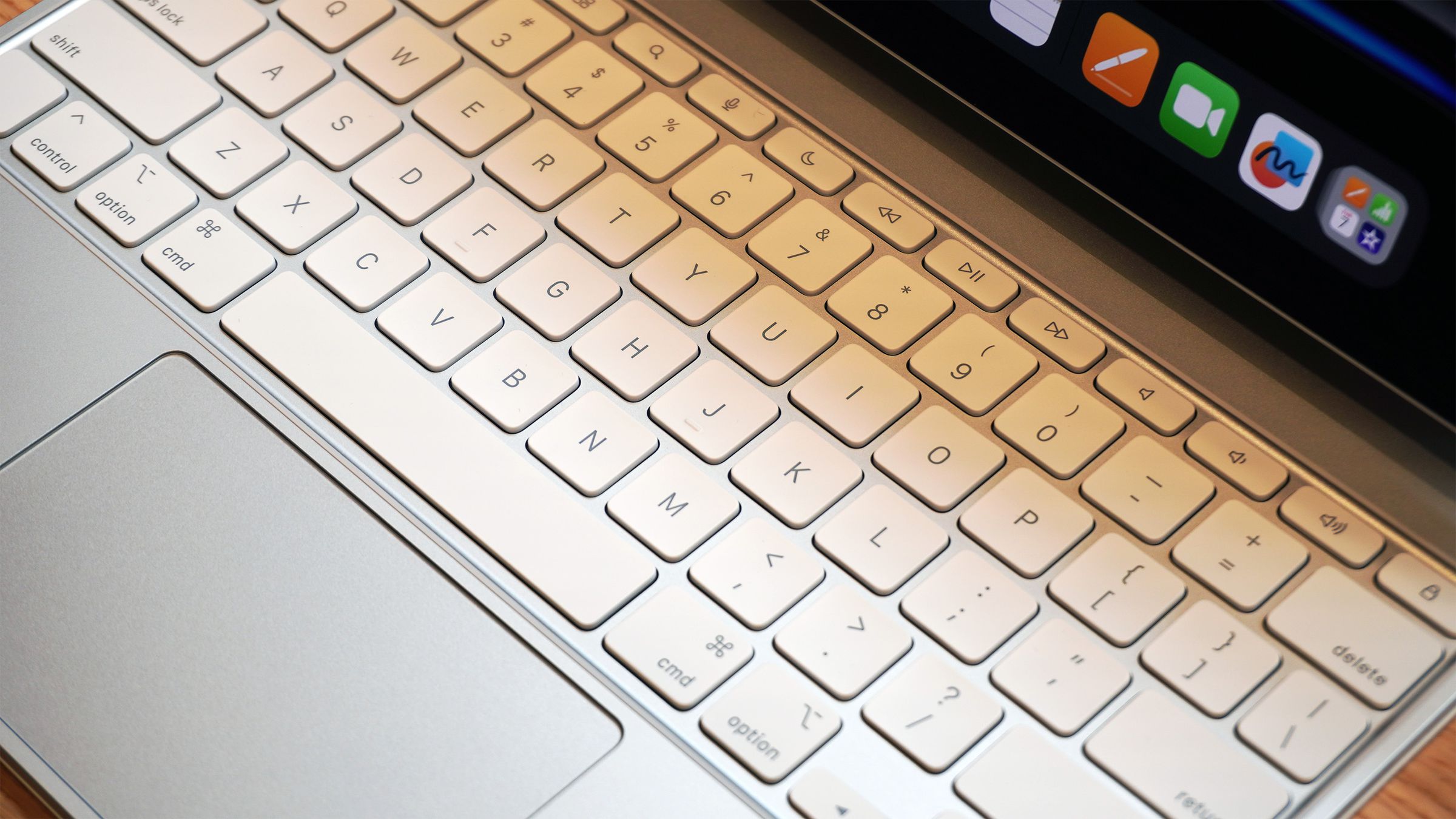 Збільшене зображення клавіатури зі сріблястою верхньою панеллю, білими клавішами та великим трекпадом. Він має функціональний ряд і підключається до iPad Pro.