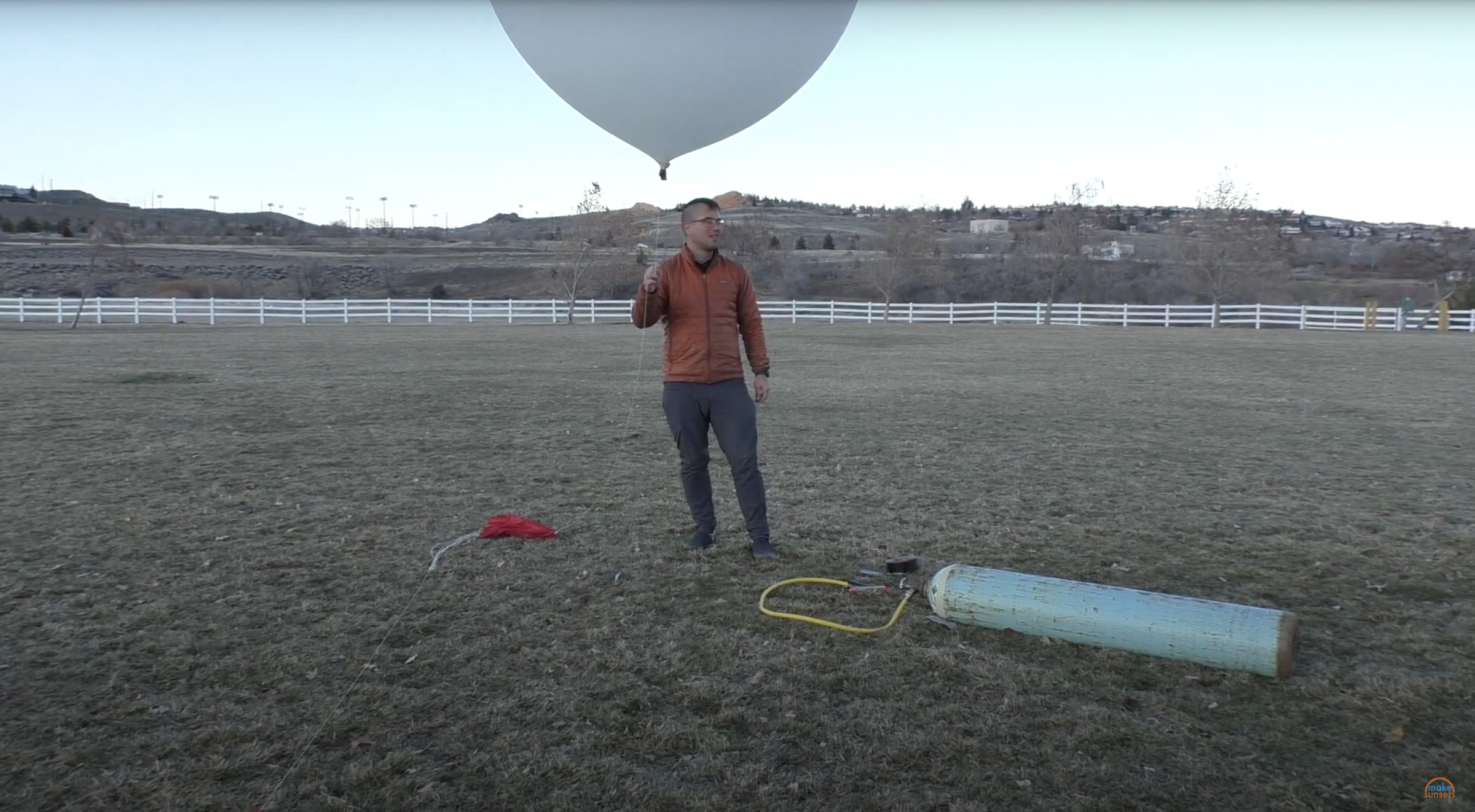 In the middle of a lawn stands a man with a large white weather balloon.