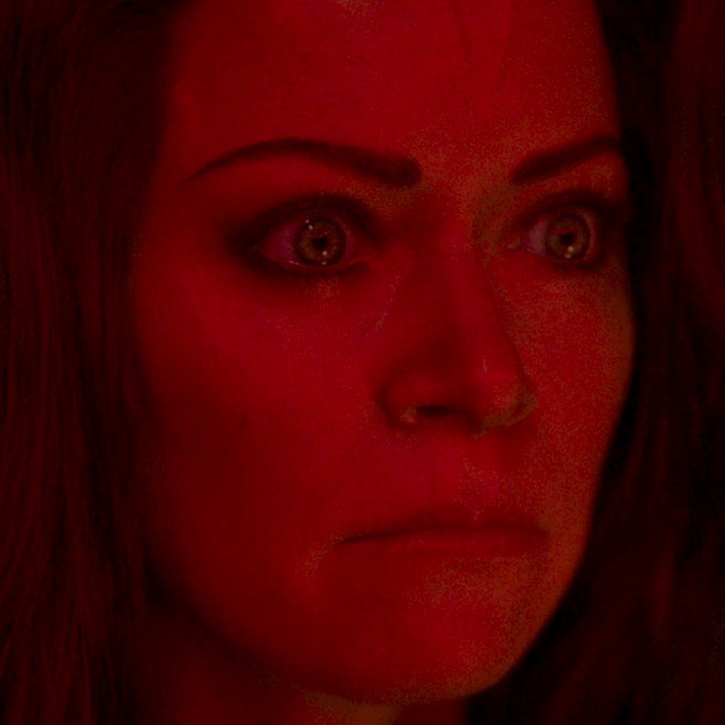 A close-up shot of a tall, green-skinned woman whose face is contorted in anger. Though the woman’s skin is green, she’s bathed in a harsh red light here that makes her look red as well.