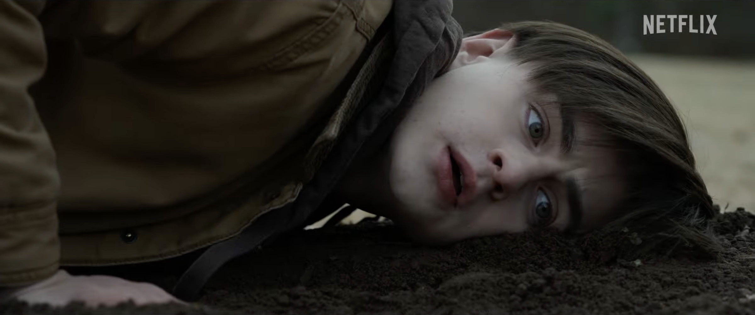 Image of a boy putting his ear to a freshly-tilled grave.