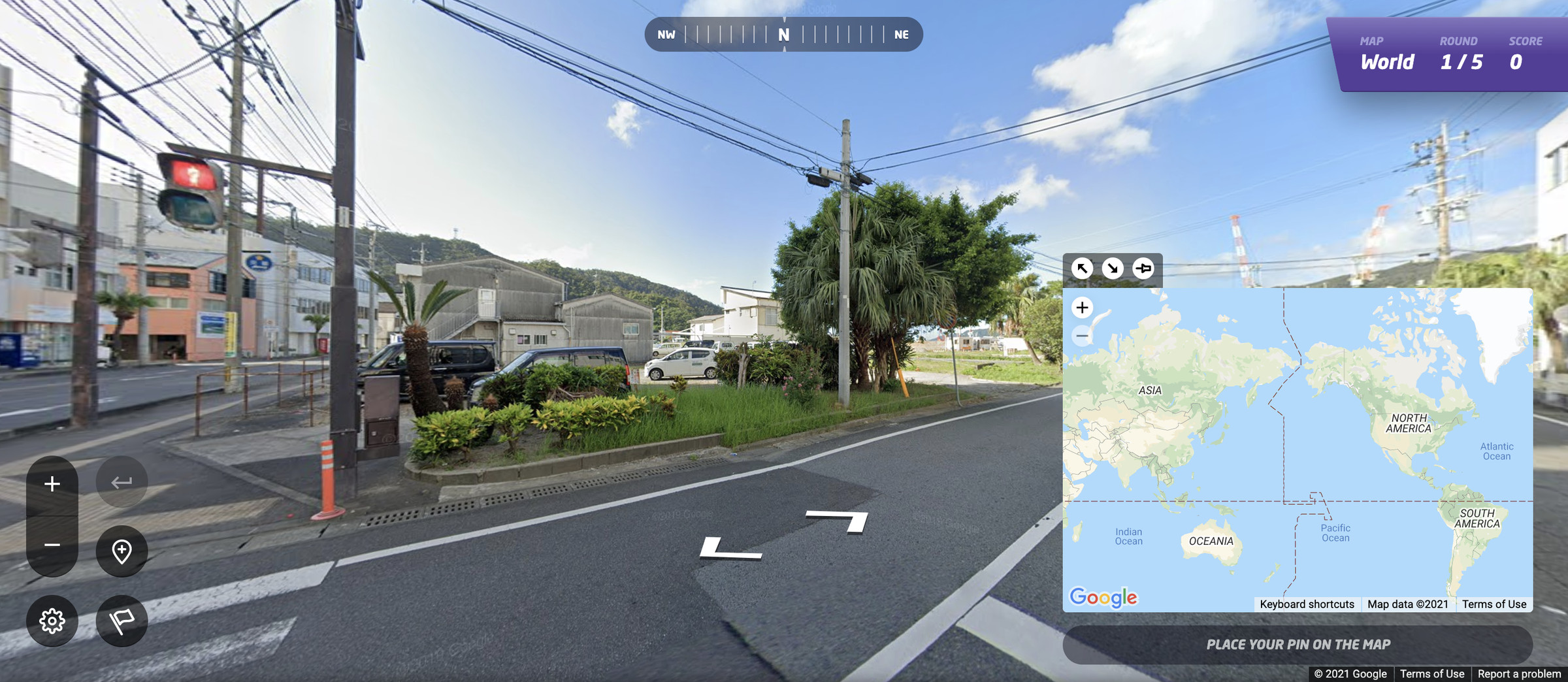 A screenshot of GeoGuessr showing a road, a tree, some buildings, and power lines. Google Street View controls let the player manipulate the game. A map in the bottom right corner lets players guess where they are.
