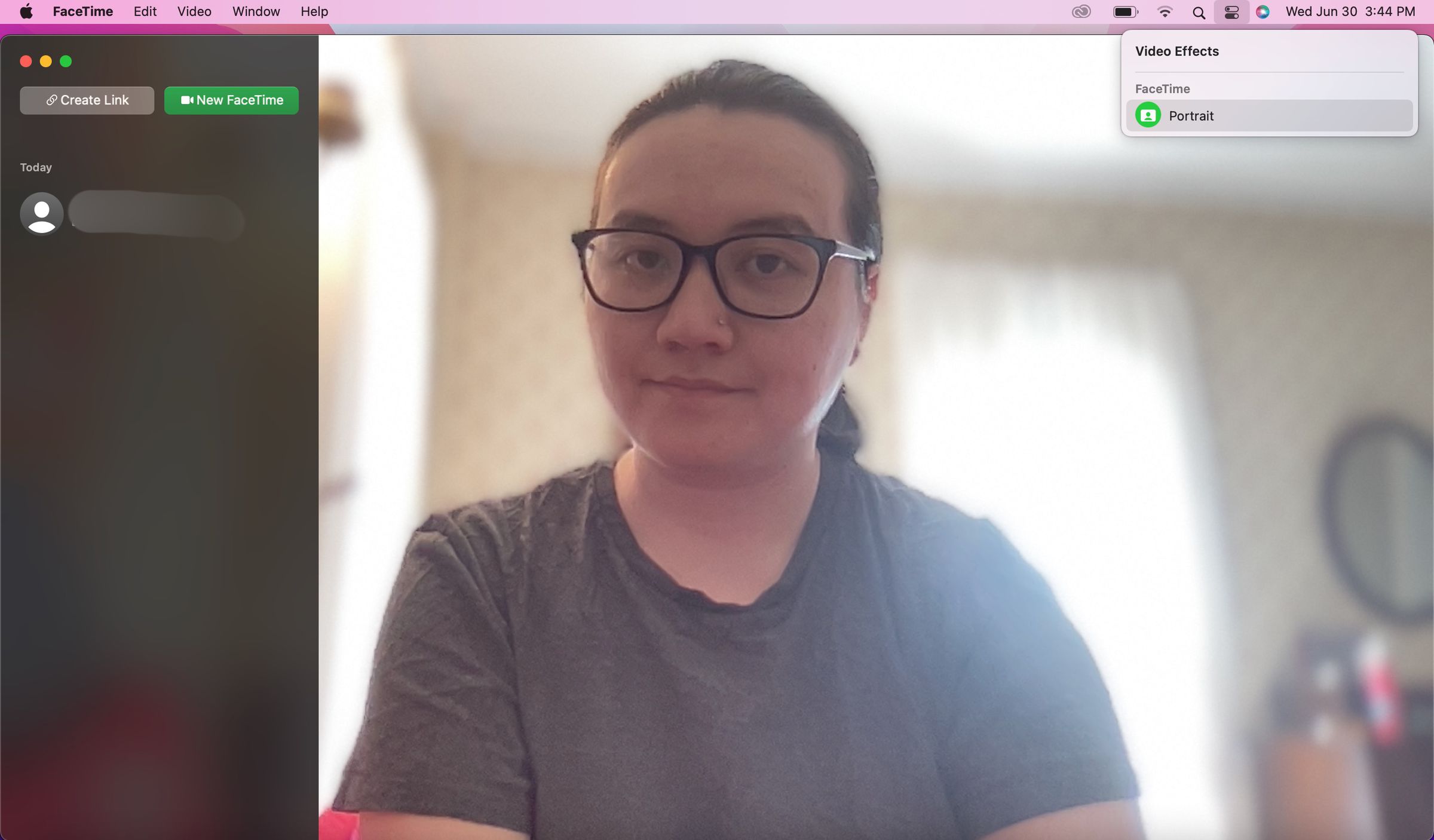 A screenshot of a MacBook screen where a user is on a FaceTime call with a blurred bright bedroom background. A FaceTime drop-down menu is open in the top right with Portrait selected.