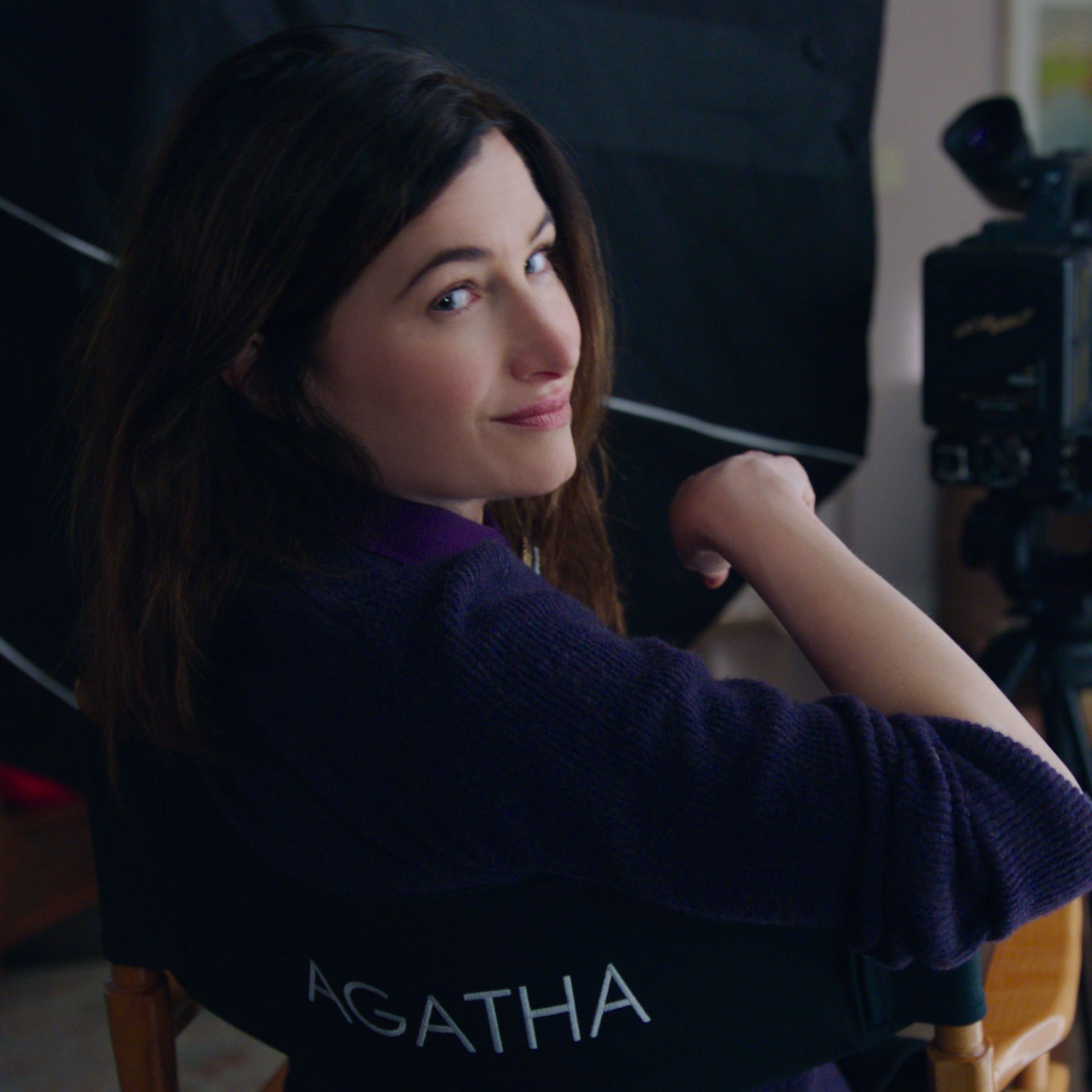 A woman in a purple shirt looking backwards over a director’s chair on a film set.