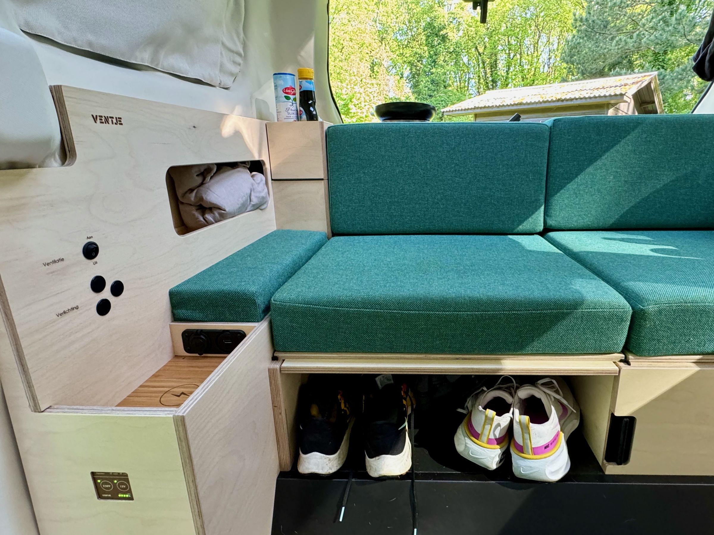 <em>On the lower left, you can control the van’s power, while the cluster of buttons above it offers control over ventilation and lighting. The dark wooden tray on the left is a wireless charging pad, which sits next to a 12V car charger and USB-A and USB-C jacks.</em>