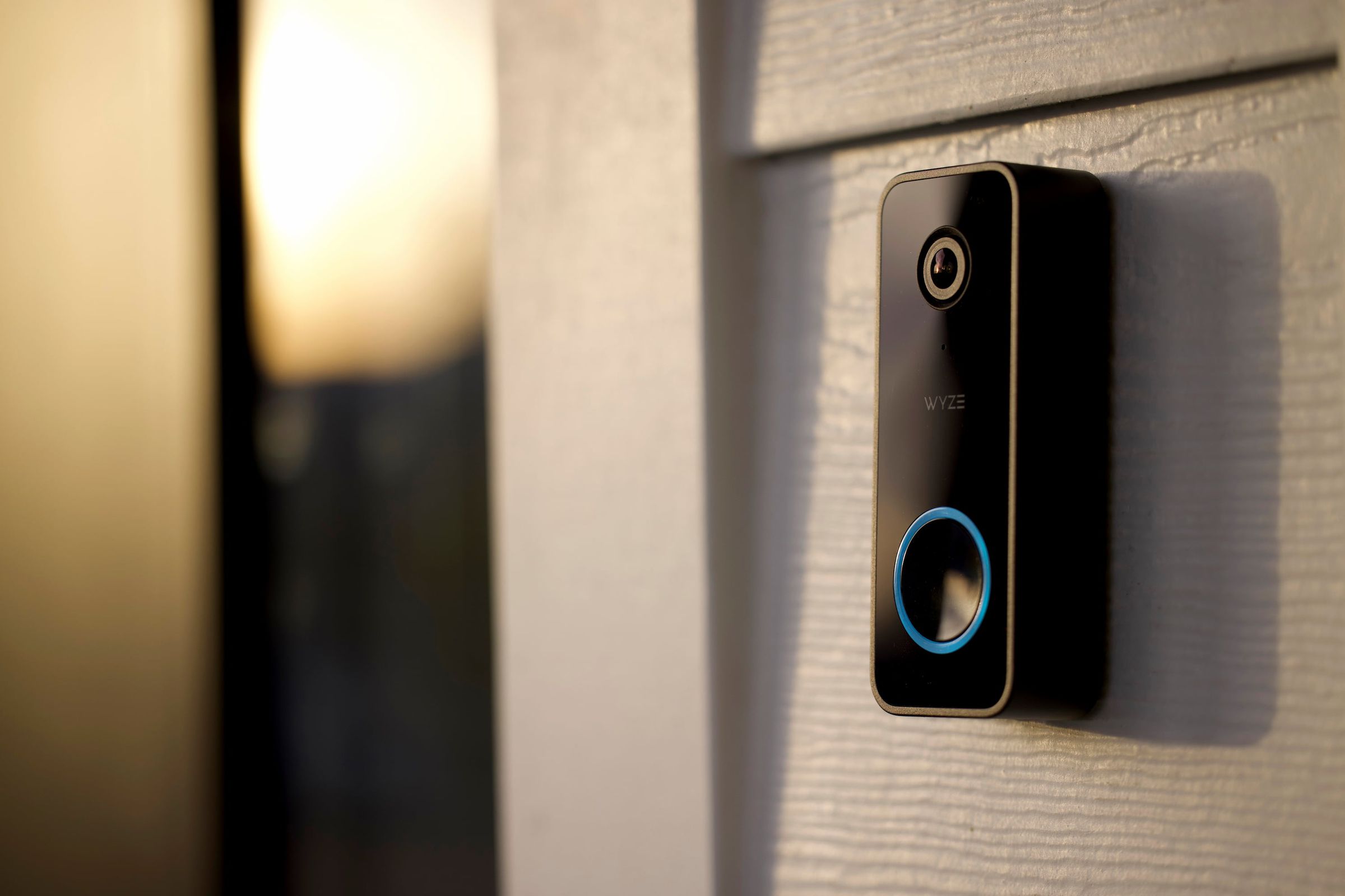 A black video doorbell with a blue LED ring next to a front door.