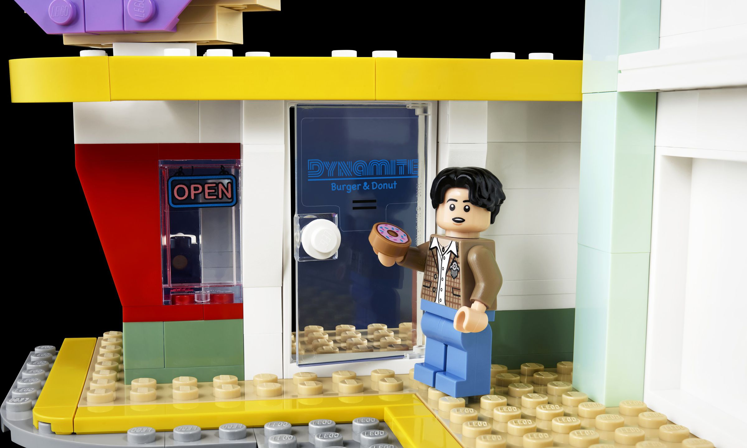 Lego figurine of Jungkook holding Lego doughnut outside a Lego doughnut shop.