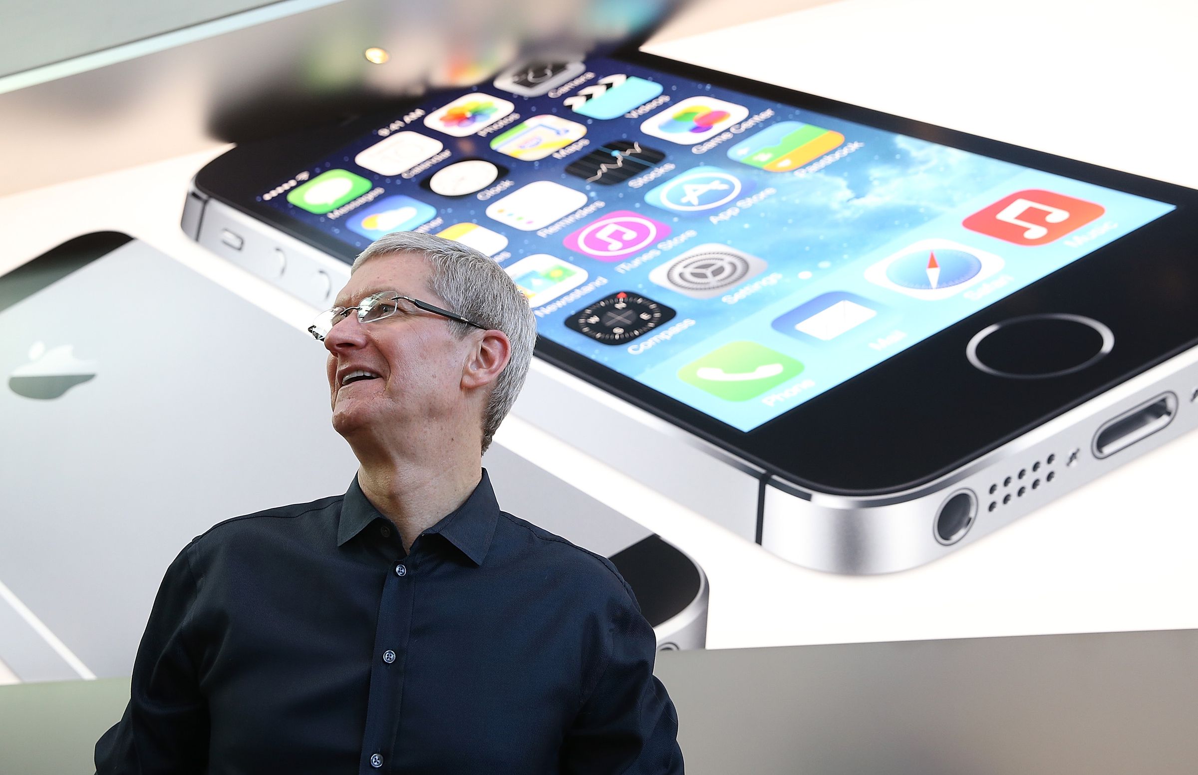 Apple CEO Tim Cook looks on at an Apple Store in front of an iPhone 5s ad.