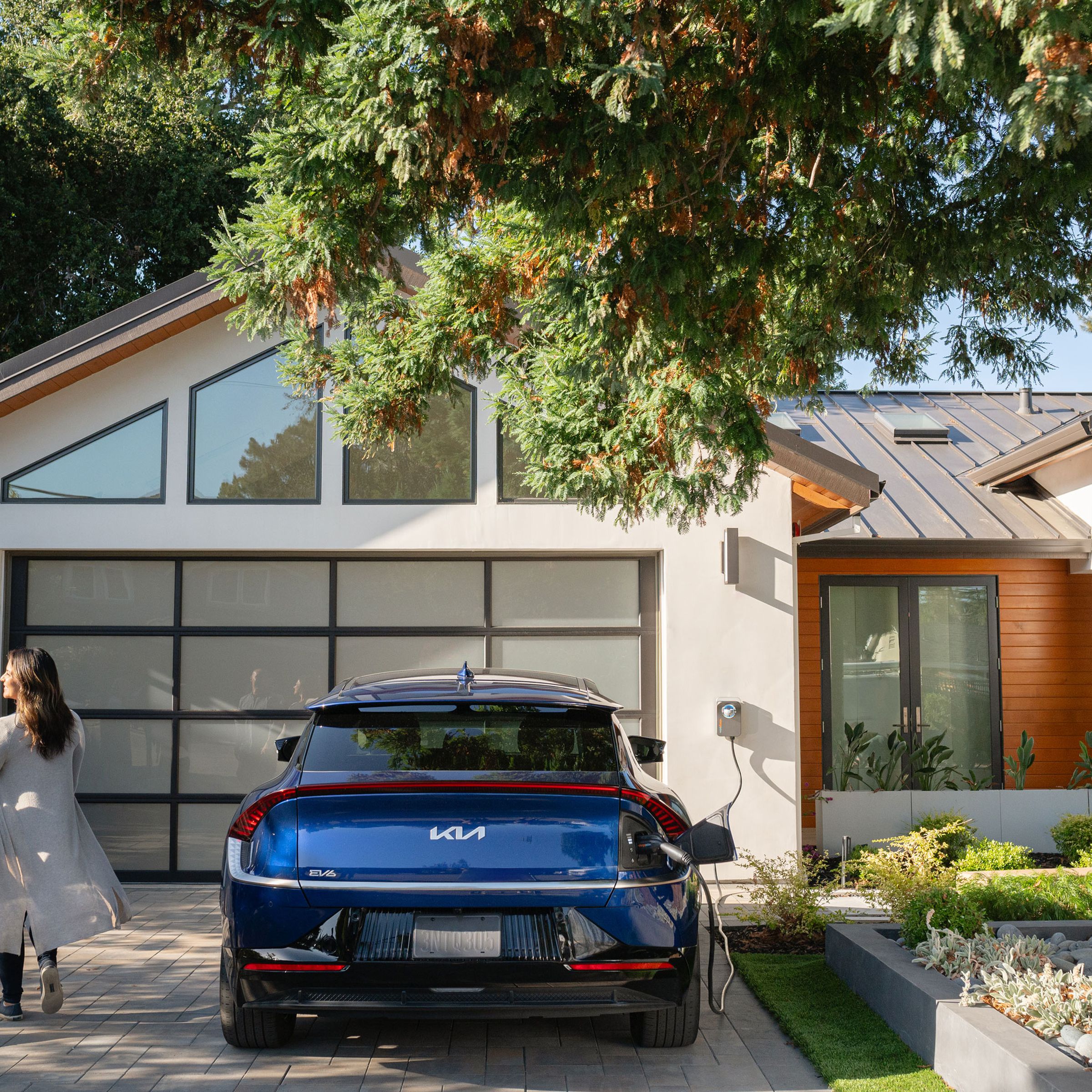 modern house with blue kia ev6 parked in front of garage with charge point charger Hooked up, and two people holding hands walking away from the car