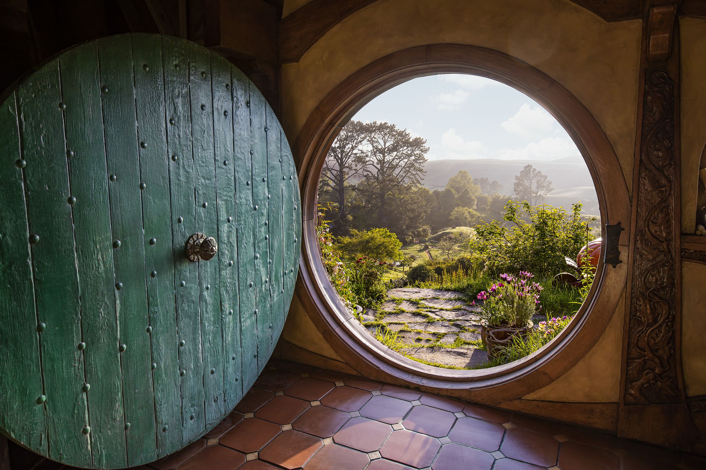 A circular Hobbit door open to reveal a green landscape that resembles The Shire from J.R.R.Tolkiens Middle Earth.