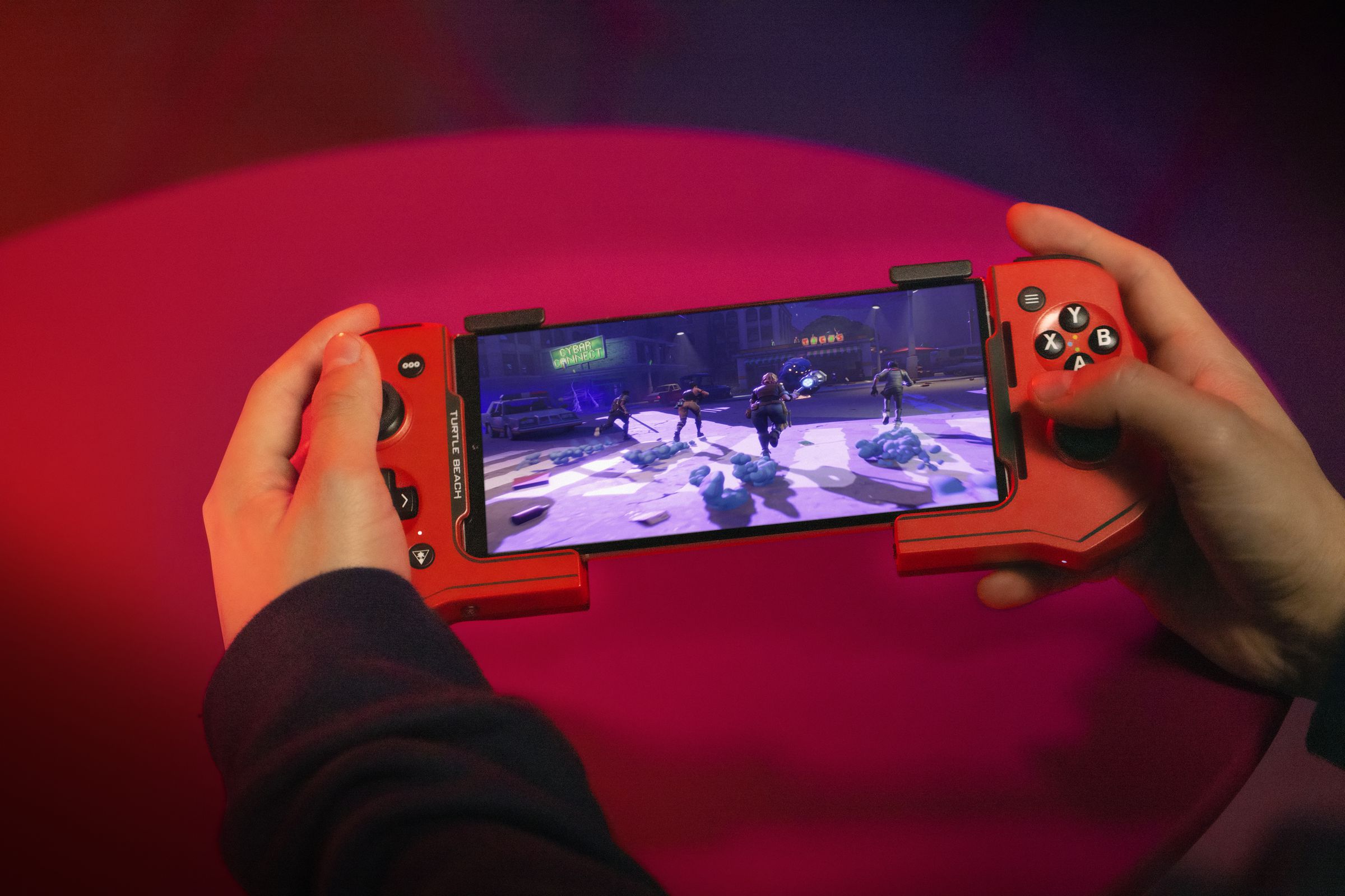 An over-the-shoulder view of a person holding the red Turtle Beach Atom phone controller with an Android smartphone mounted within it, playing a game.