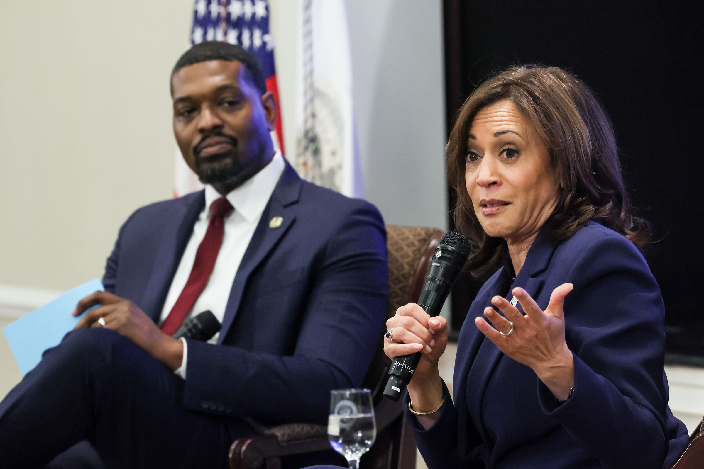 Kamala Harris speaks into a microphone, with Michael Regan sitting next to her.