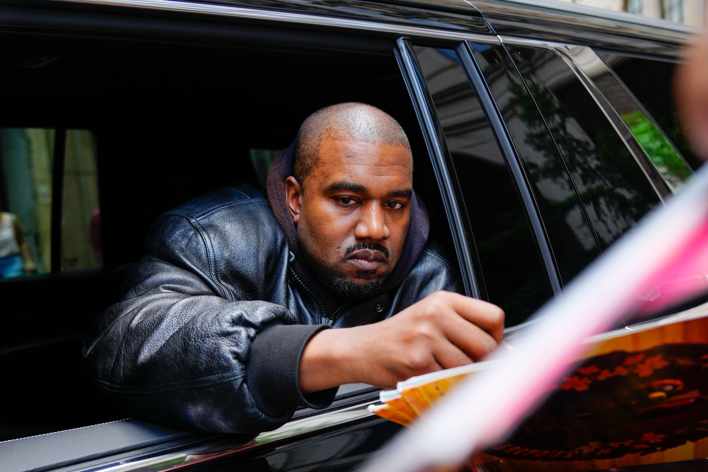 A photo of Kanye West signing an autograph outside of a car window