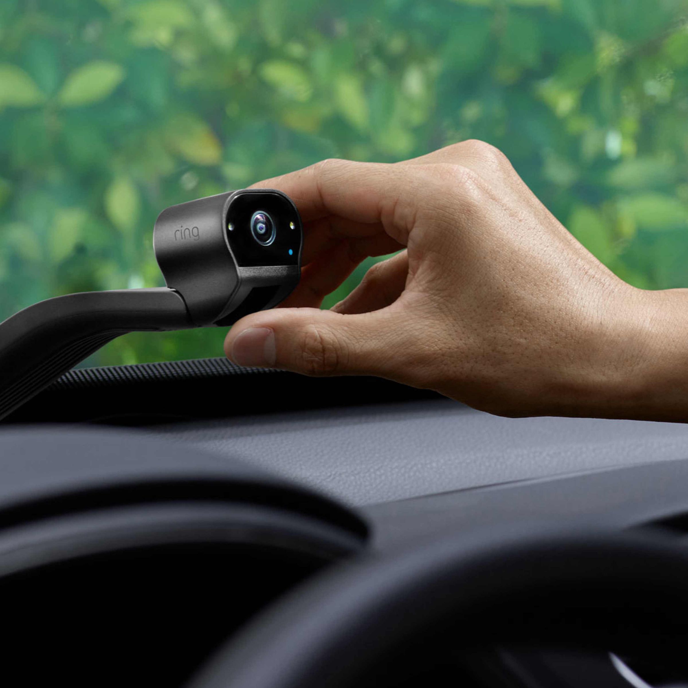 A small camera on a car windscreen with a hand adjusting it.