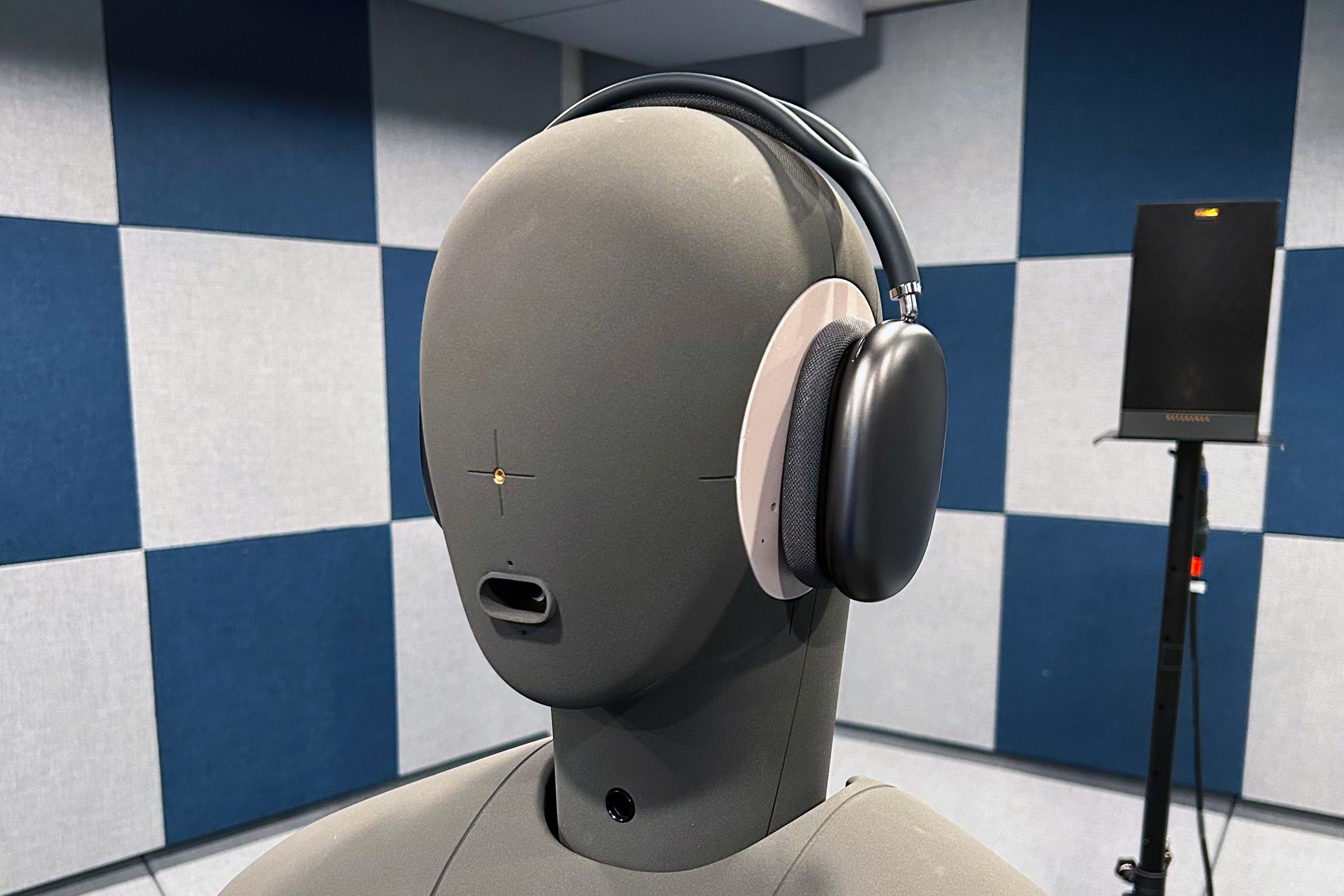 A pair of Apple AirPods Max headphones on a gray dummy head in a soundproof room.