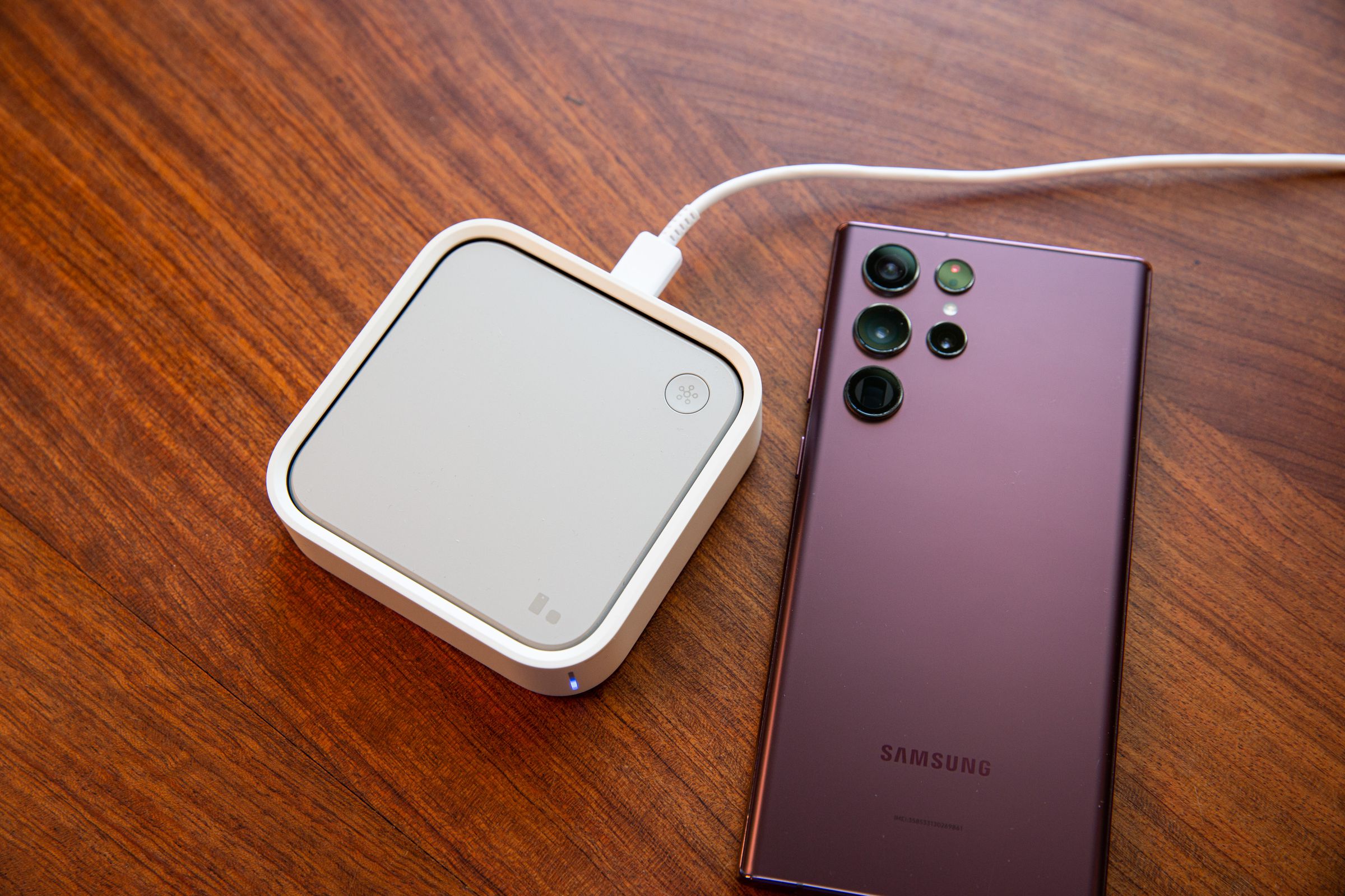 Square white SmartThings hub next to a smartphone.